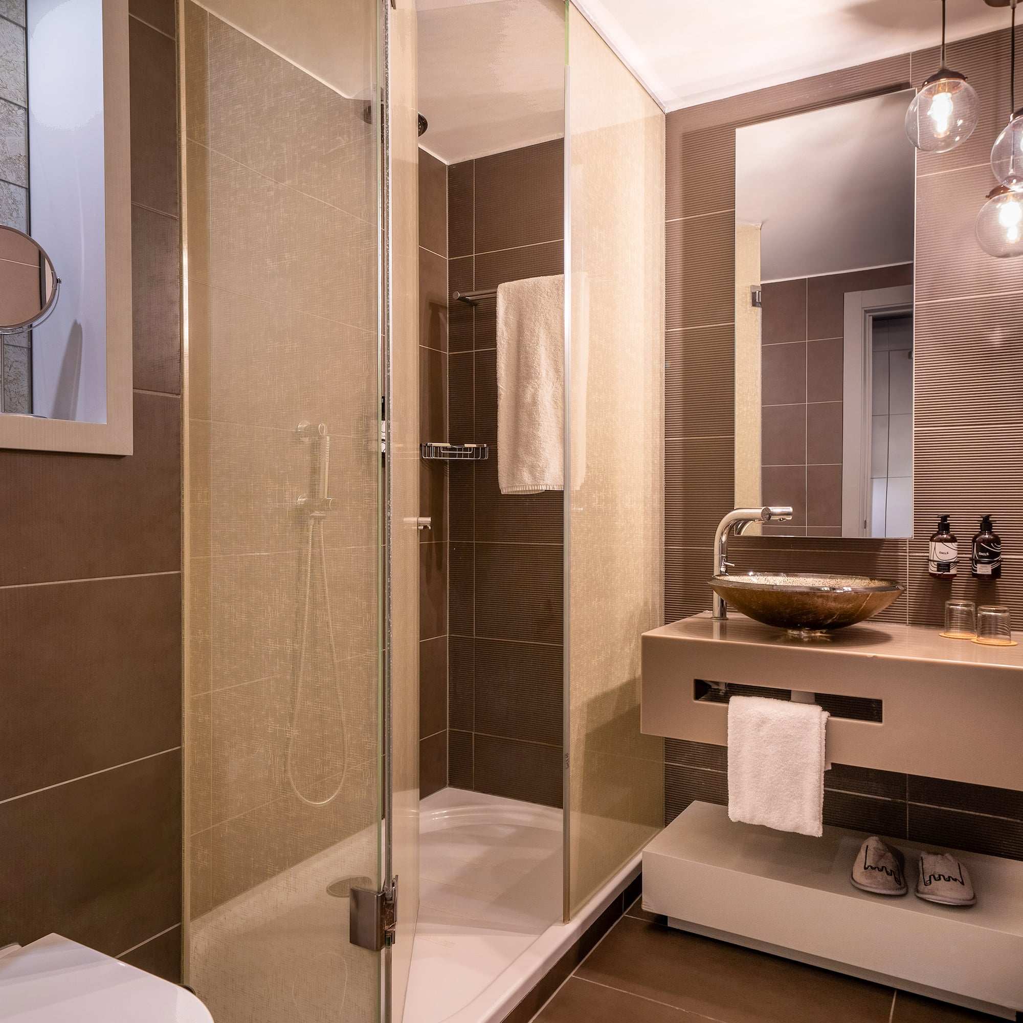 Modern brown-tiled bathroom with glass shower, floating vanity, and mirror.
