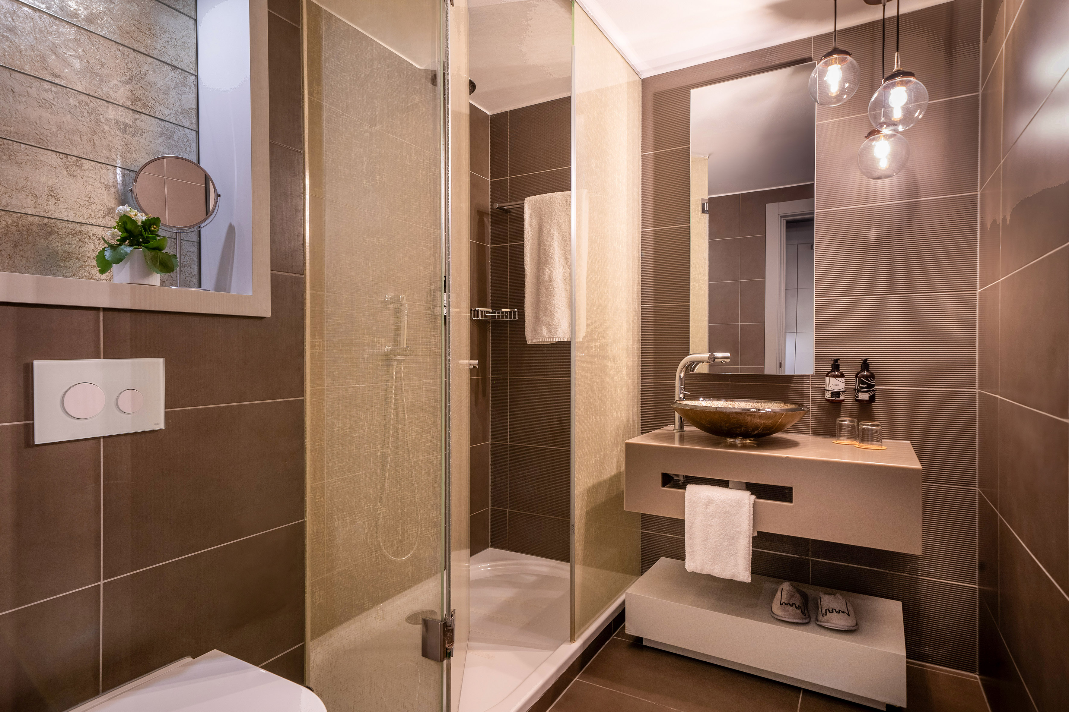 Modern brown-tiled bathroom with glass shower, floating vanity, and mirror.
