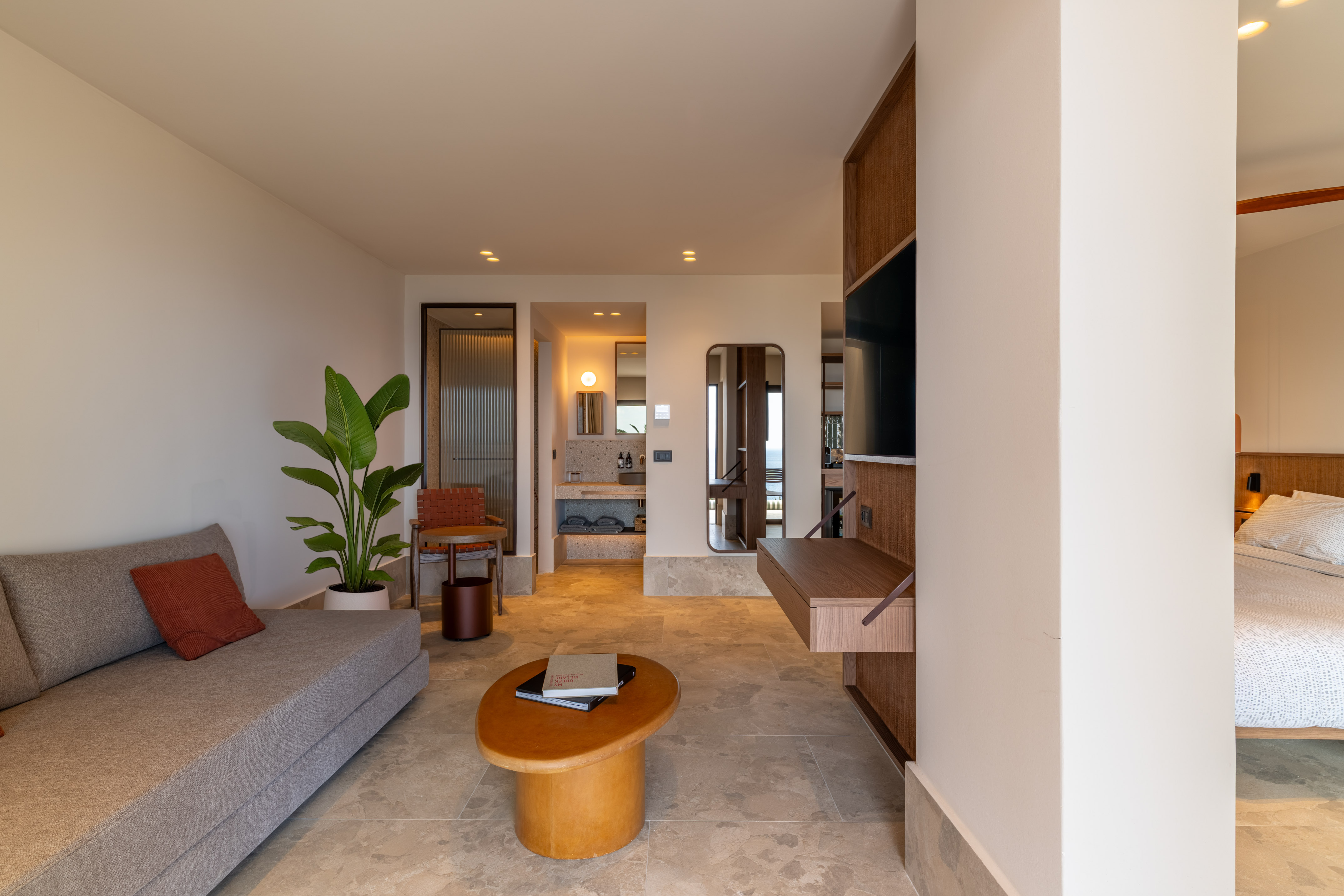 Contemporary suite: sofa, coffee table, plant, with bedroom and bath visible.