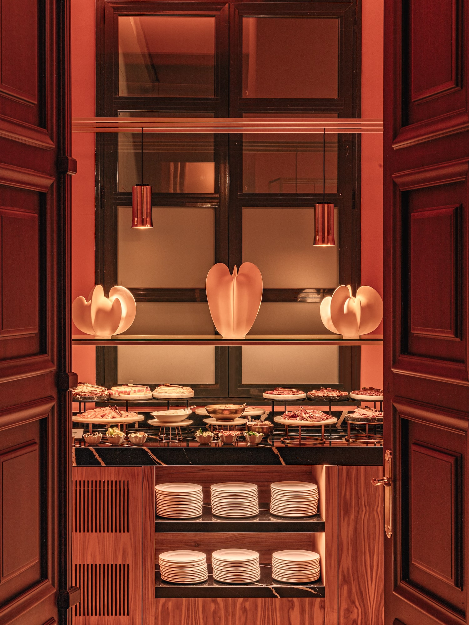 Warm-lit elegant buffet with appetizers, stacked plates, and stylish decor.