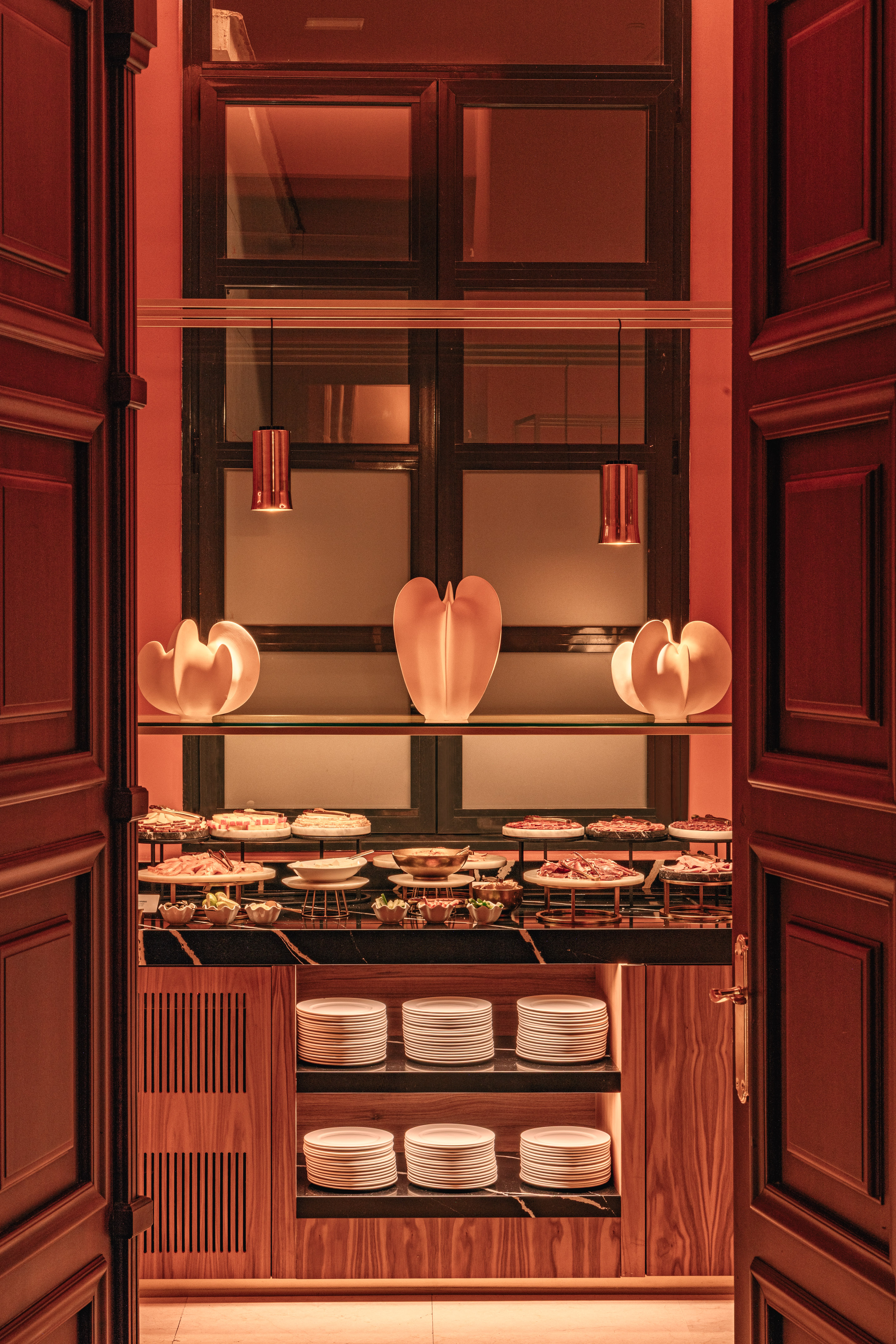 Warm-lit elegant buffet with appetizers, stacked plates, and stylish decor.