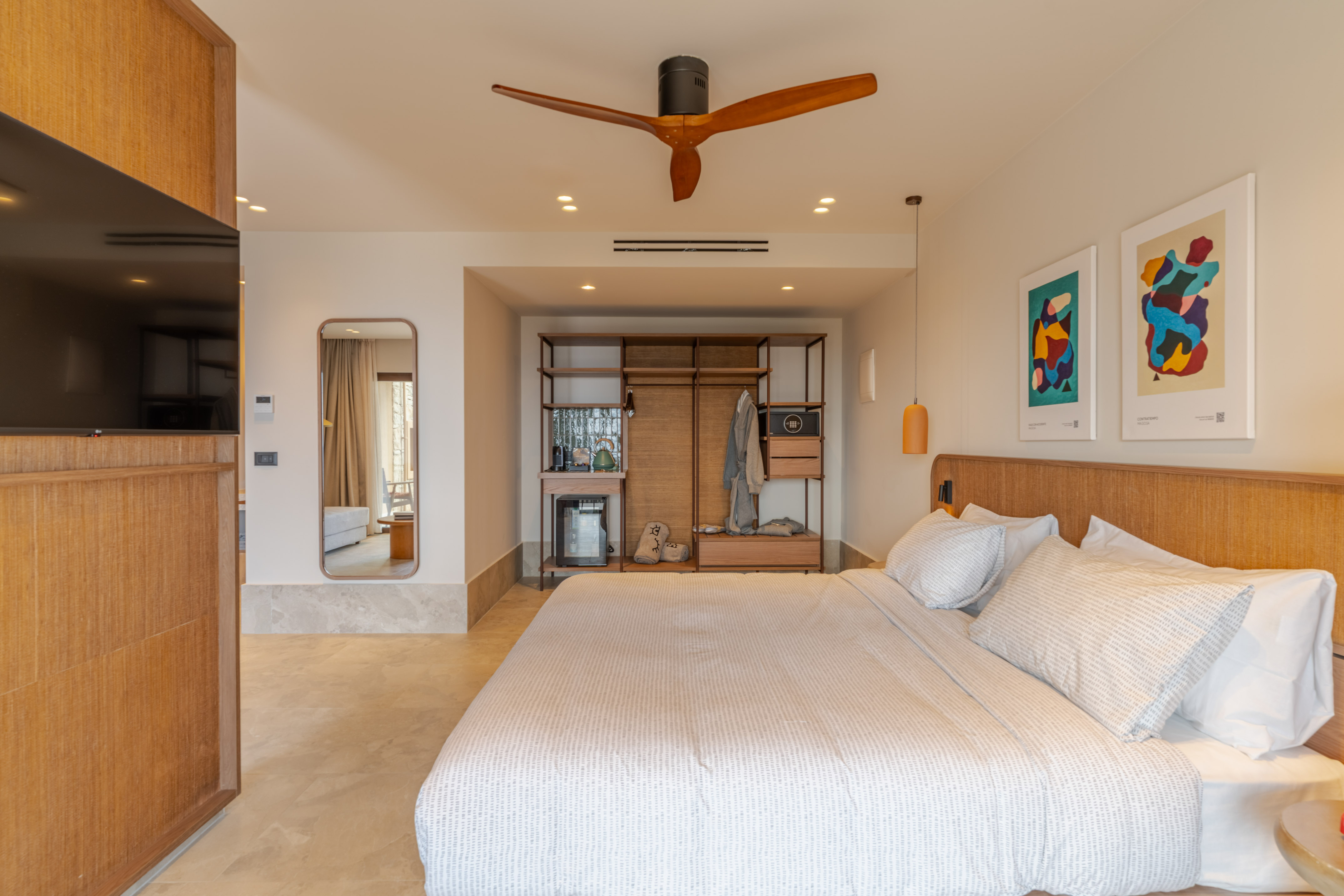 Modern hotel bedroom with large bed, wooden ceiling fan, and open wardrobe.