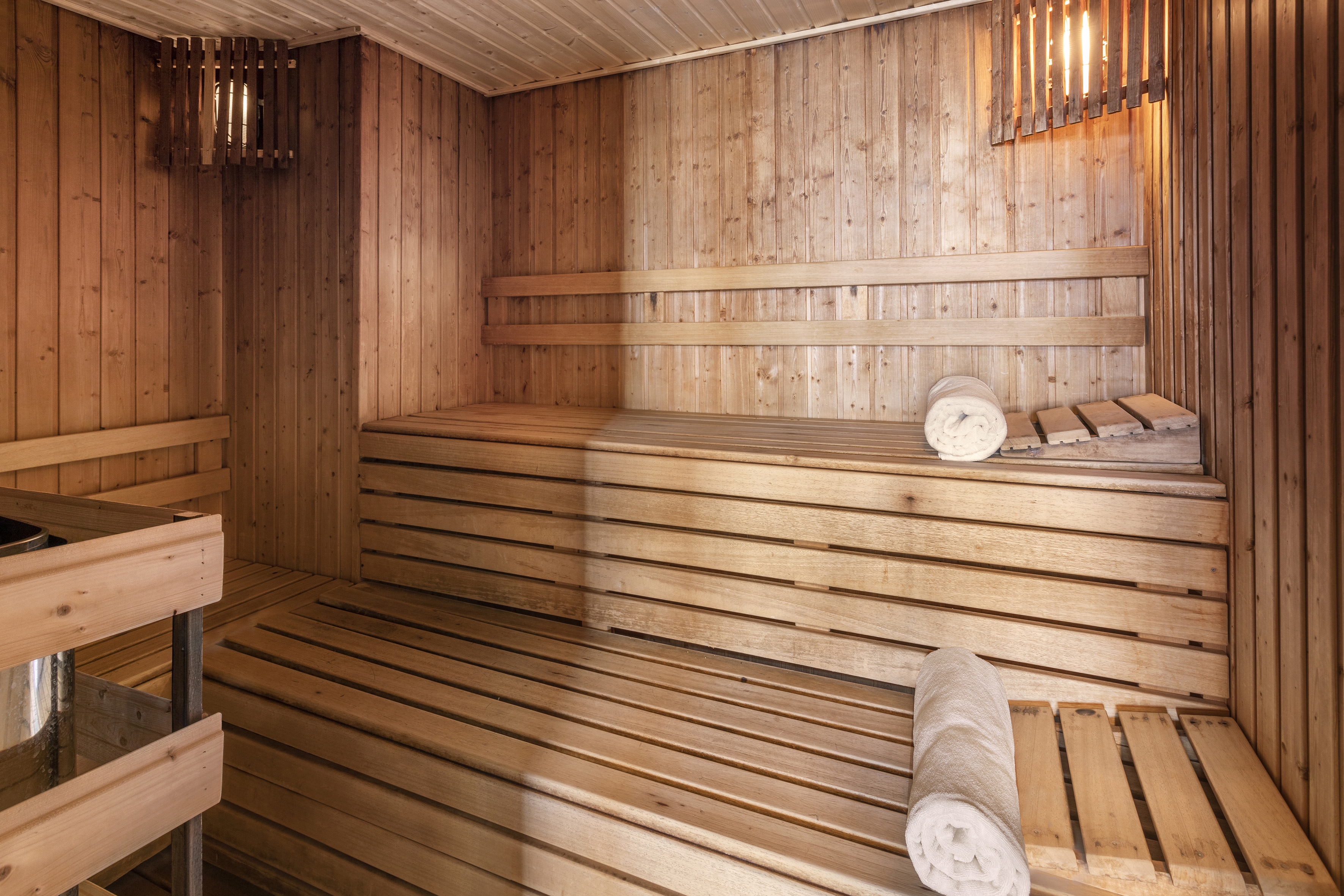 Traditional wooden sauna interior with tiered benches, warm lighting, and white towels.