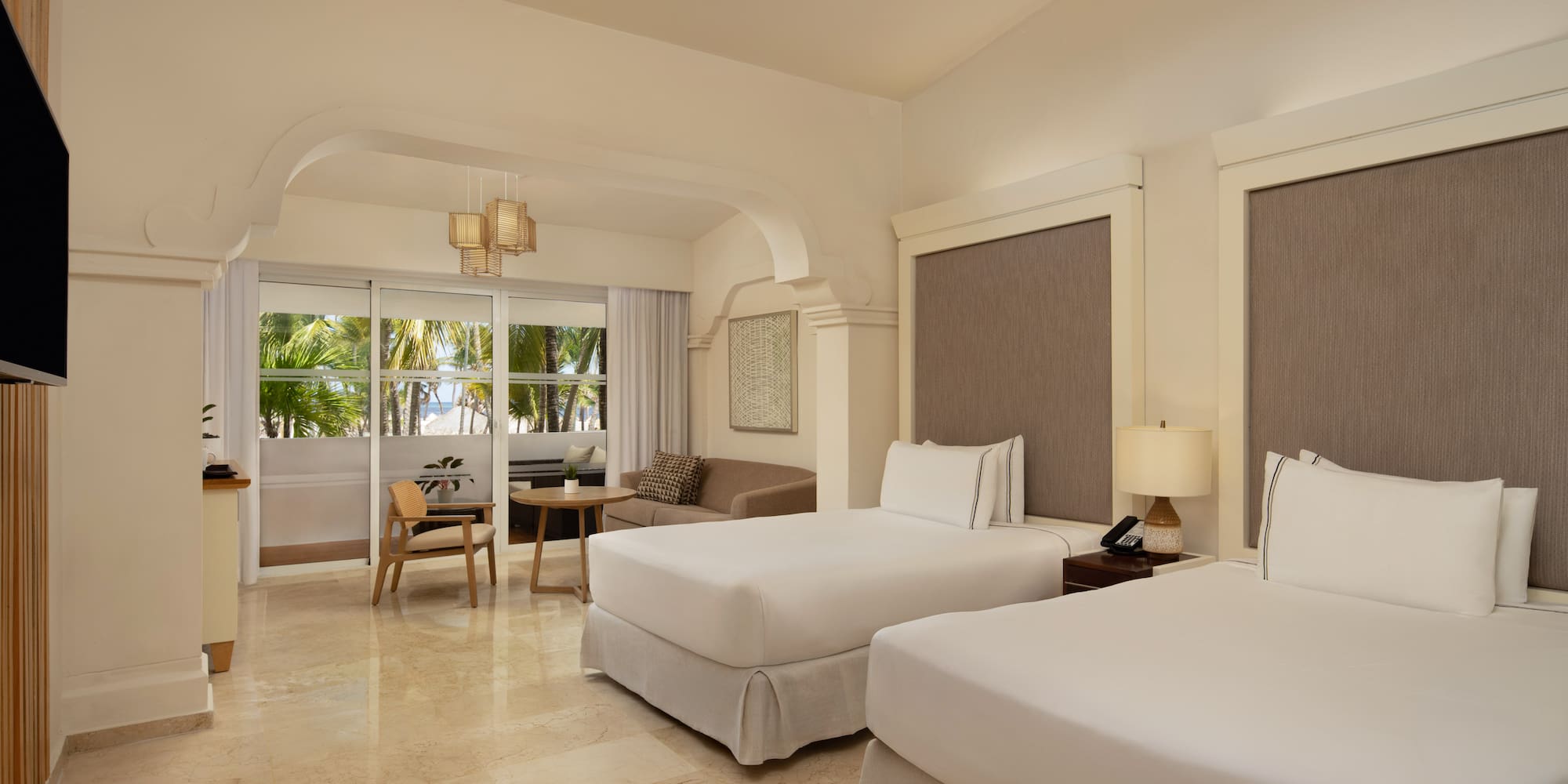 Resort bedroom with twin beds, sitting area, and tropical ocean view.