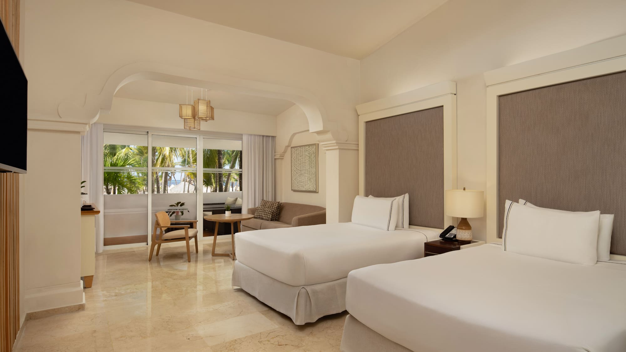Resort bedroom with twin beds, sitting area, and tropical ocean view.