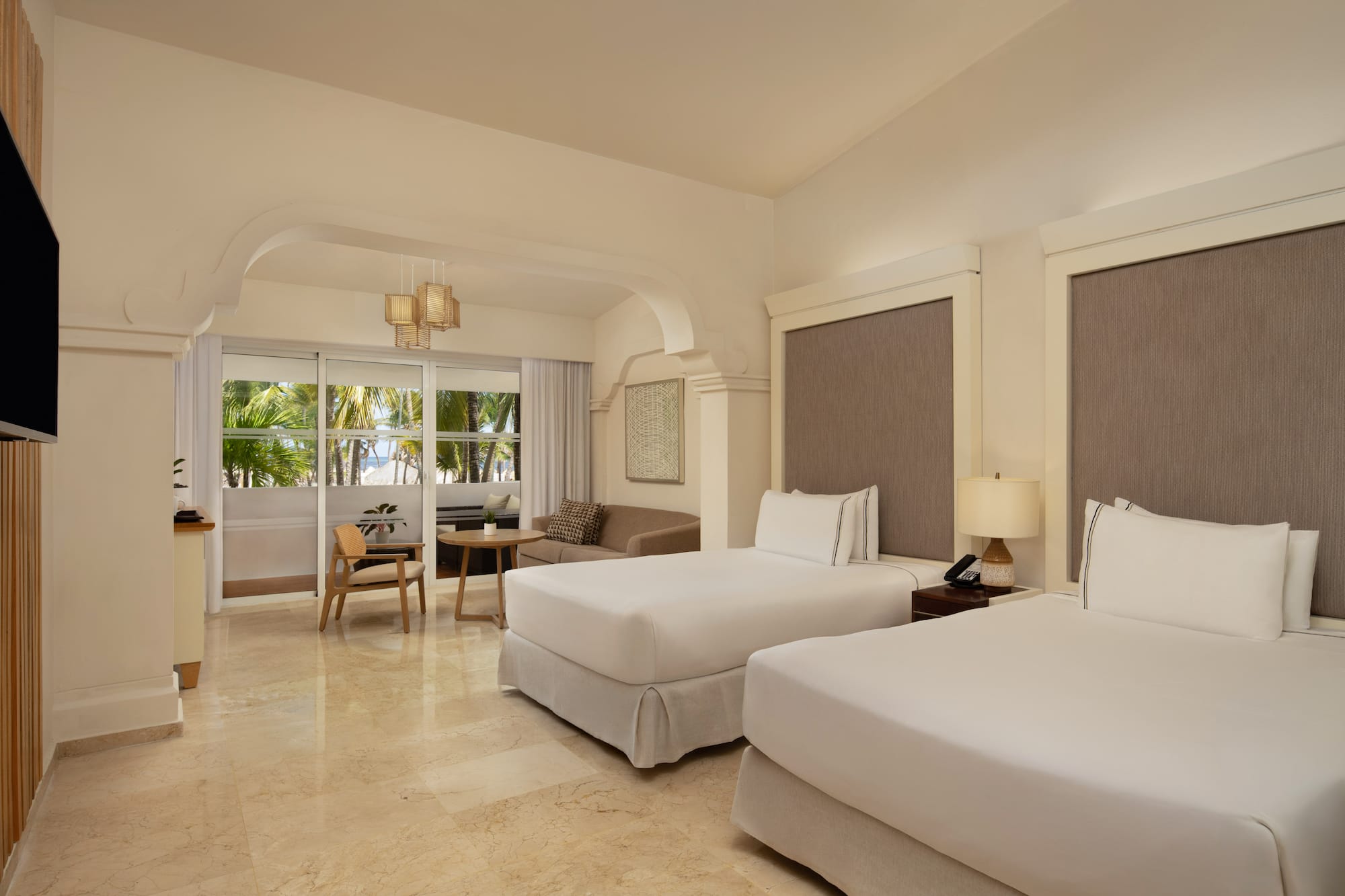 Resort bedroom with twin beds, sitting area, and tropical ocean view.