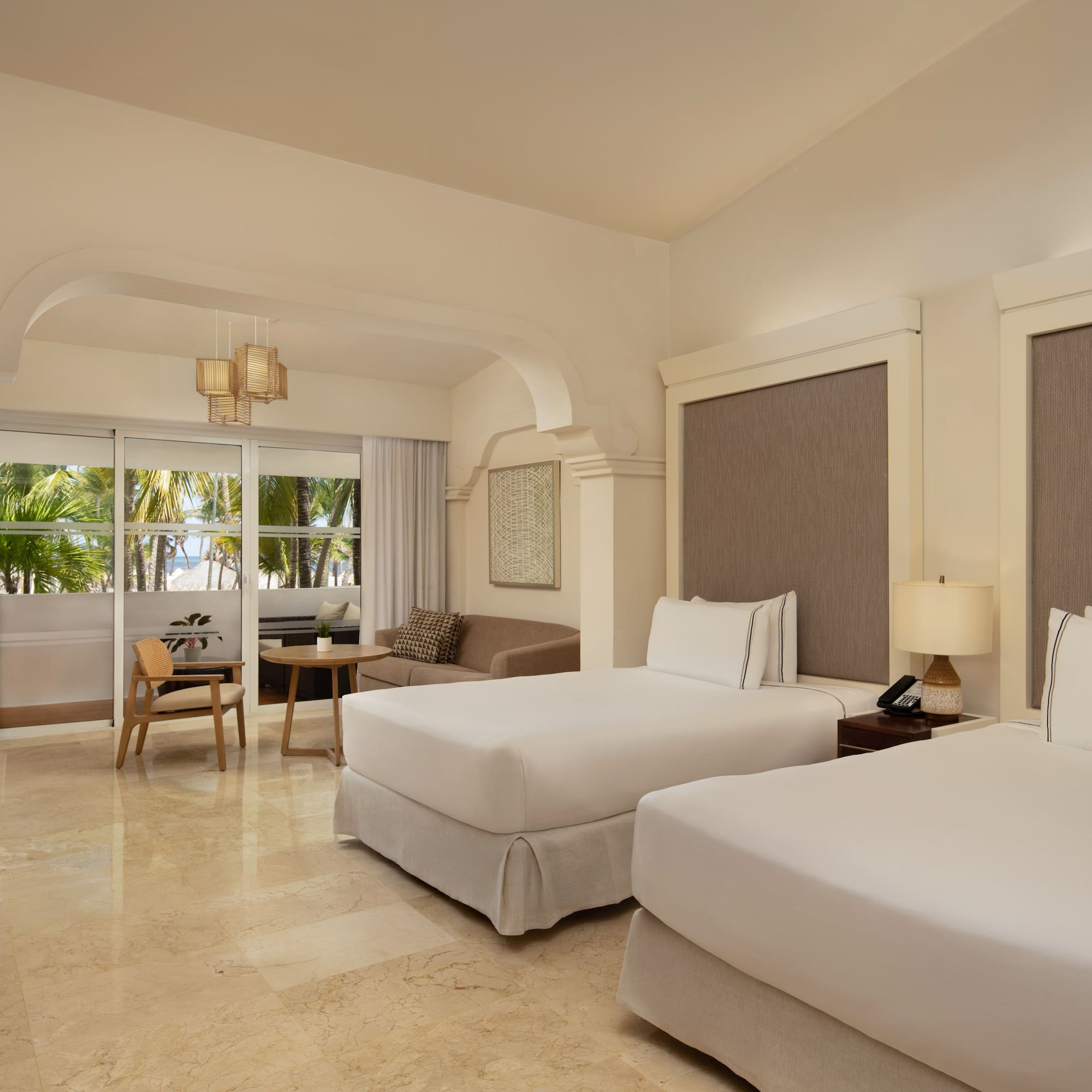 Resort bedroom with twin beds, sitting area, and tropical ocean view.