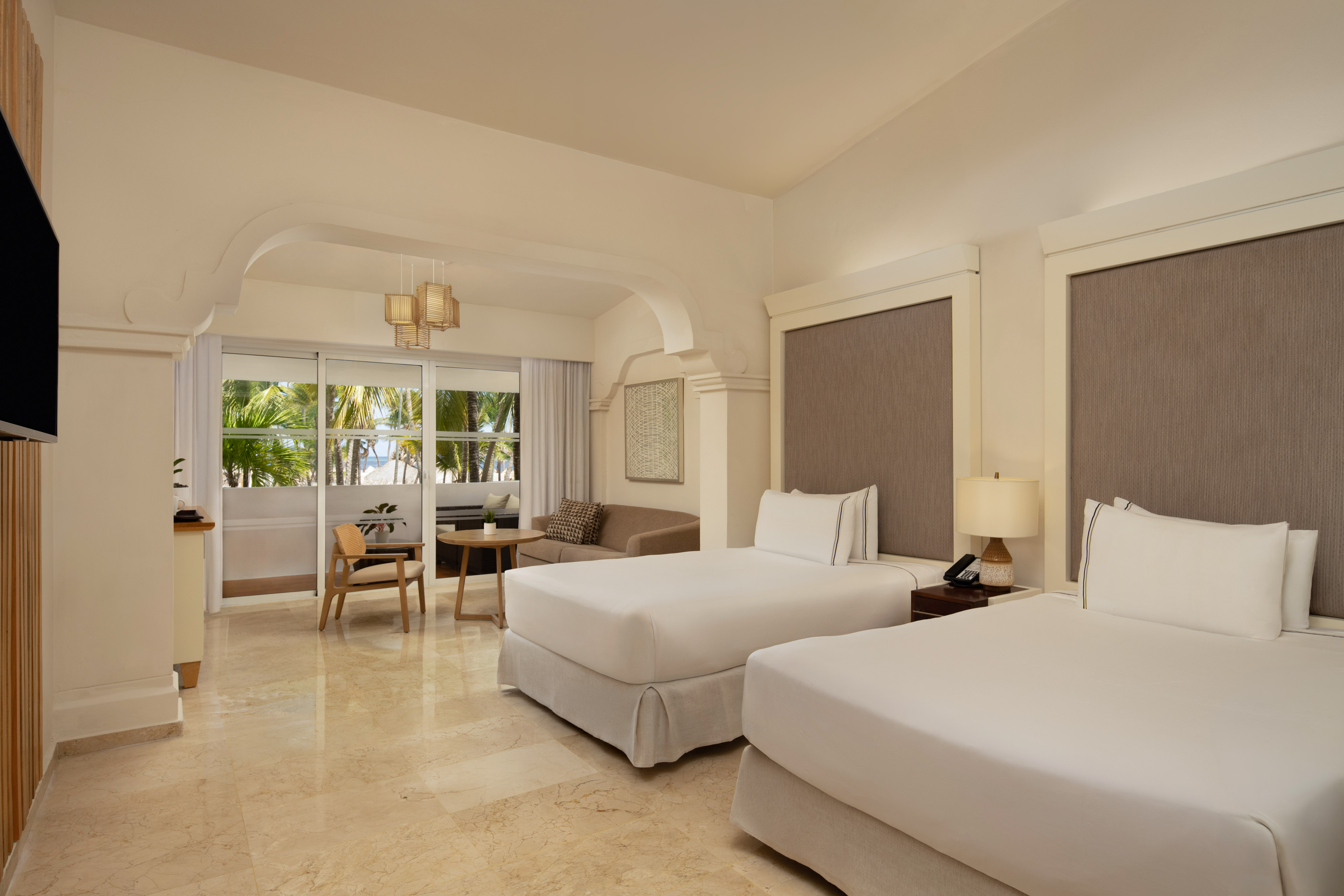 Resort bedroom with twin beds, sitting area, and tropical ocean view.