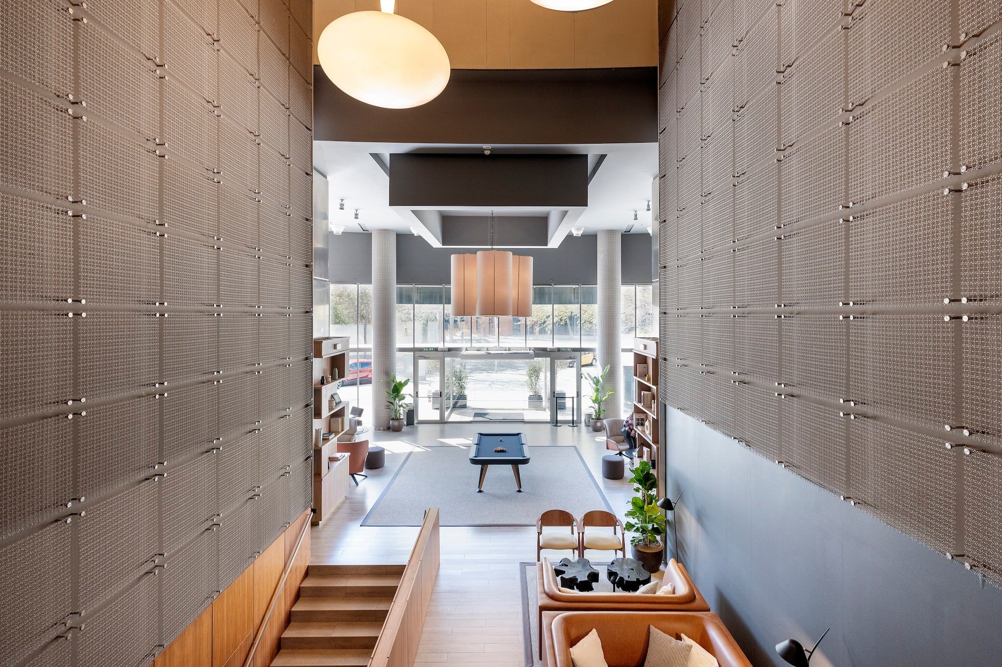 Modern lobby with pool table, leather seating, high ceilings, and textured walls.