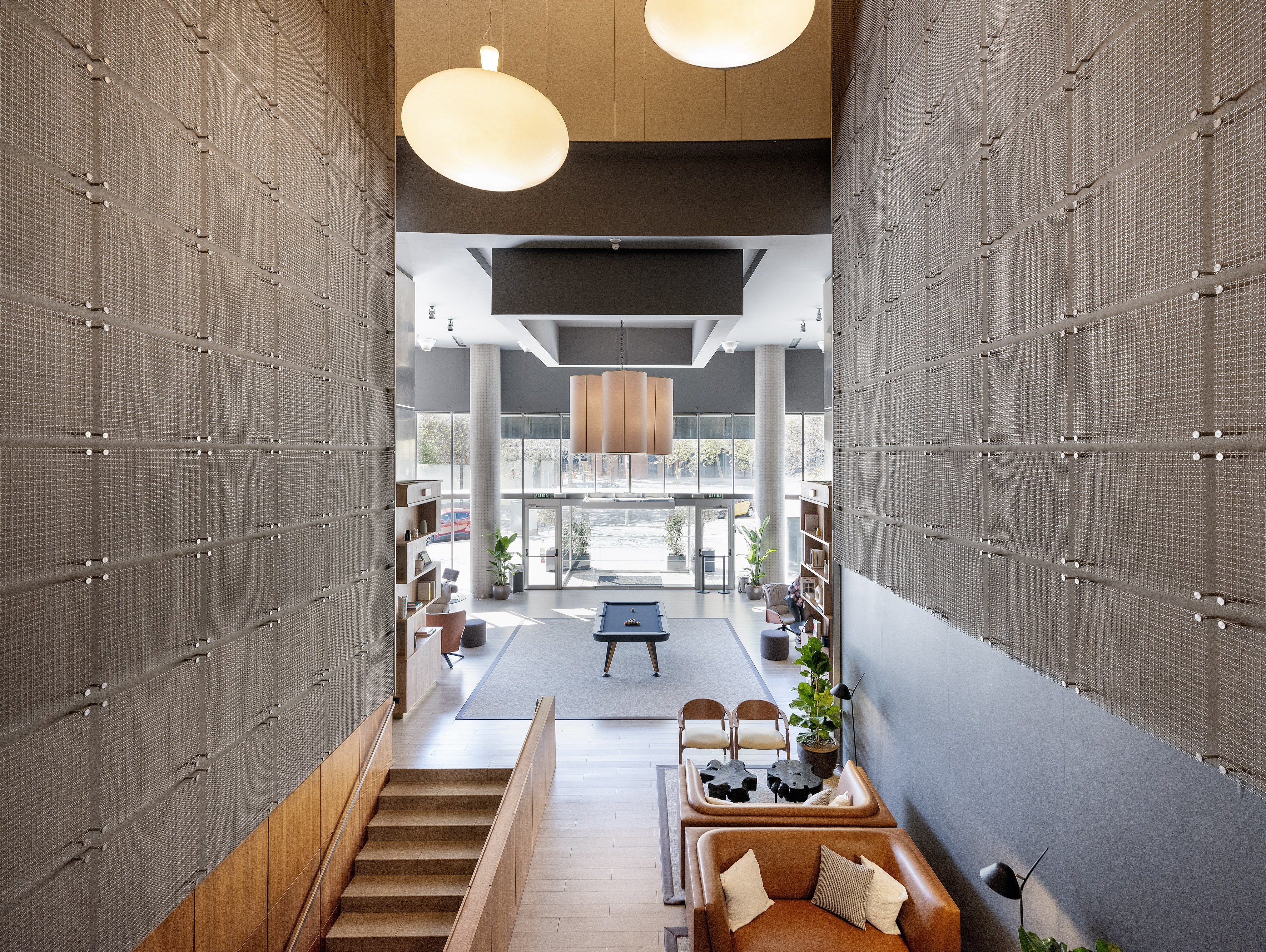 Modern lobby with pool table, leather seating, high ceilings, and textured walls.