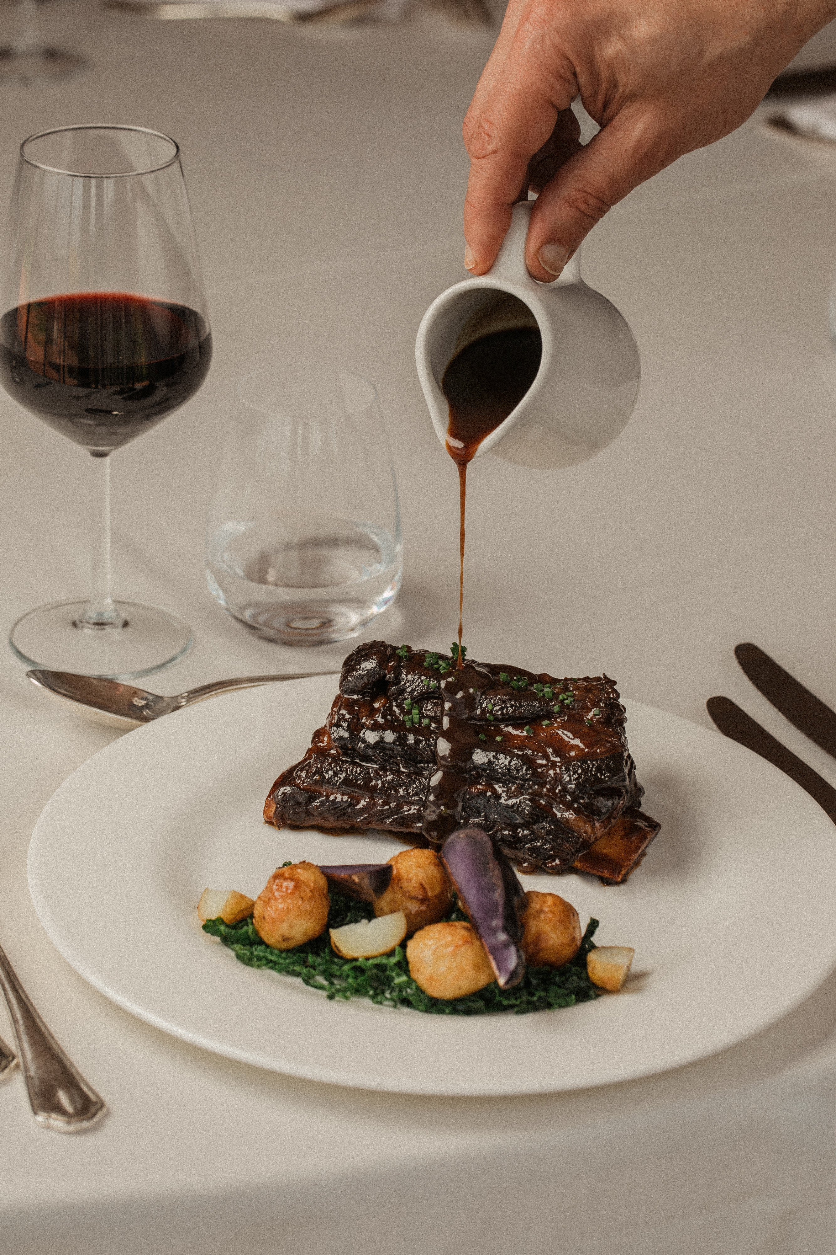 Braised short ribs with potatoes and greens, hand pouring gravy, red wine.