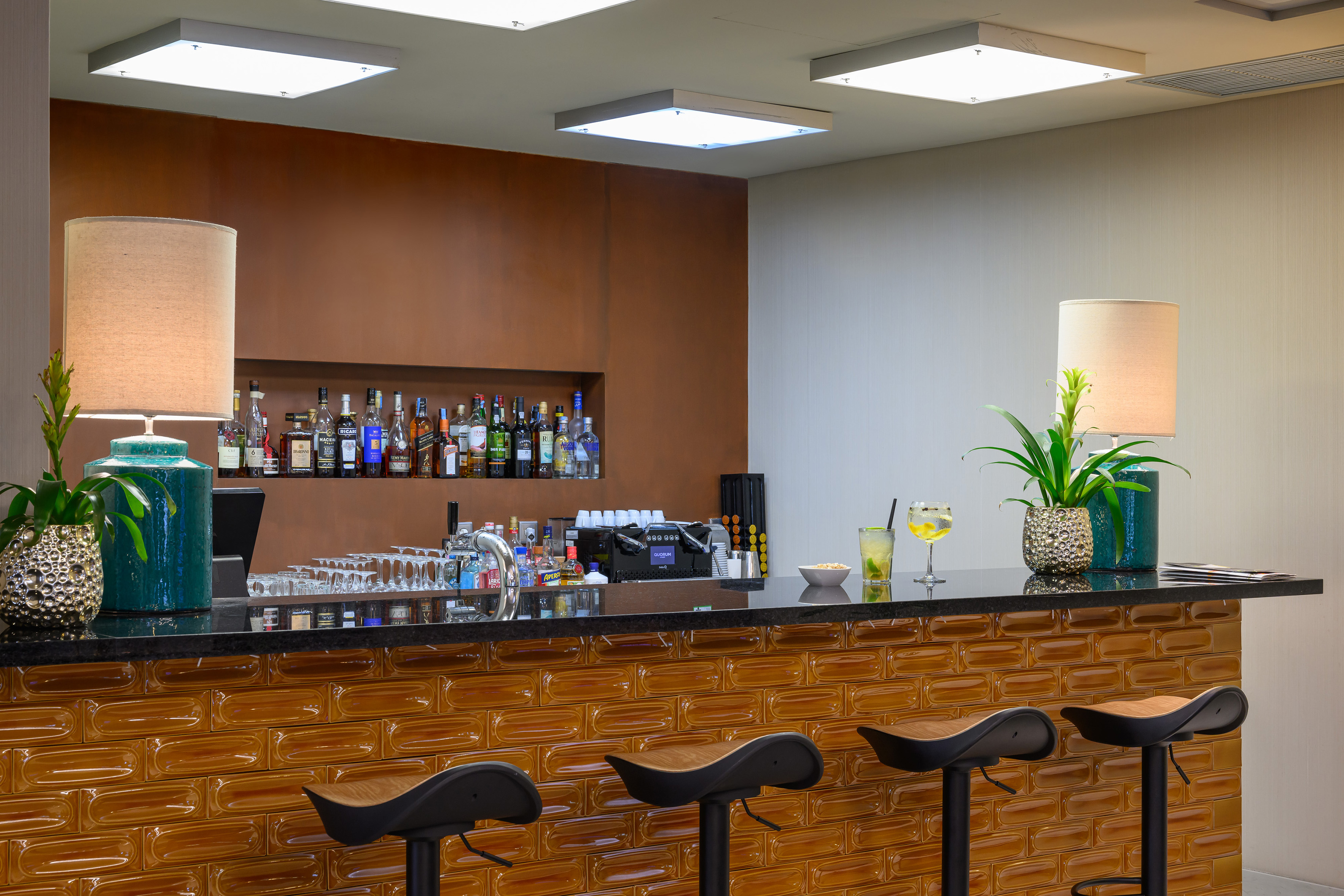 Stylish bar with glossy brown subway tiles, black stools, liquor, and cocktails.