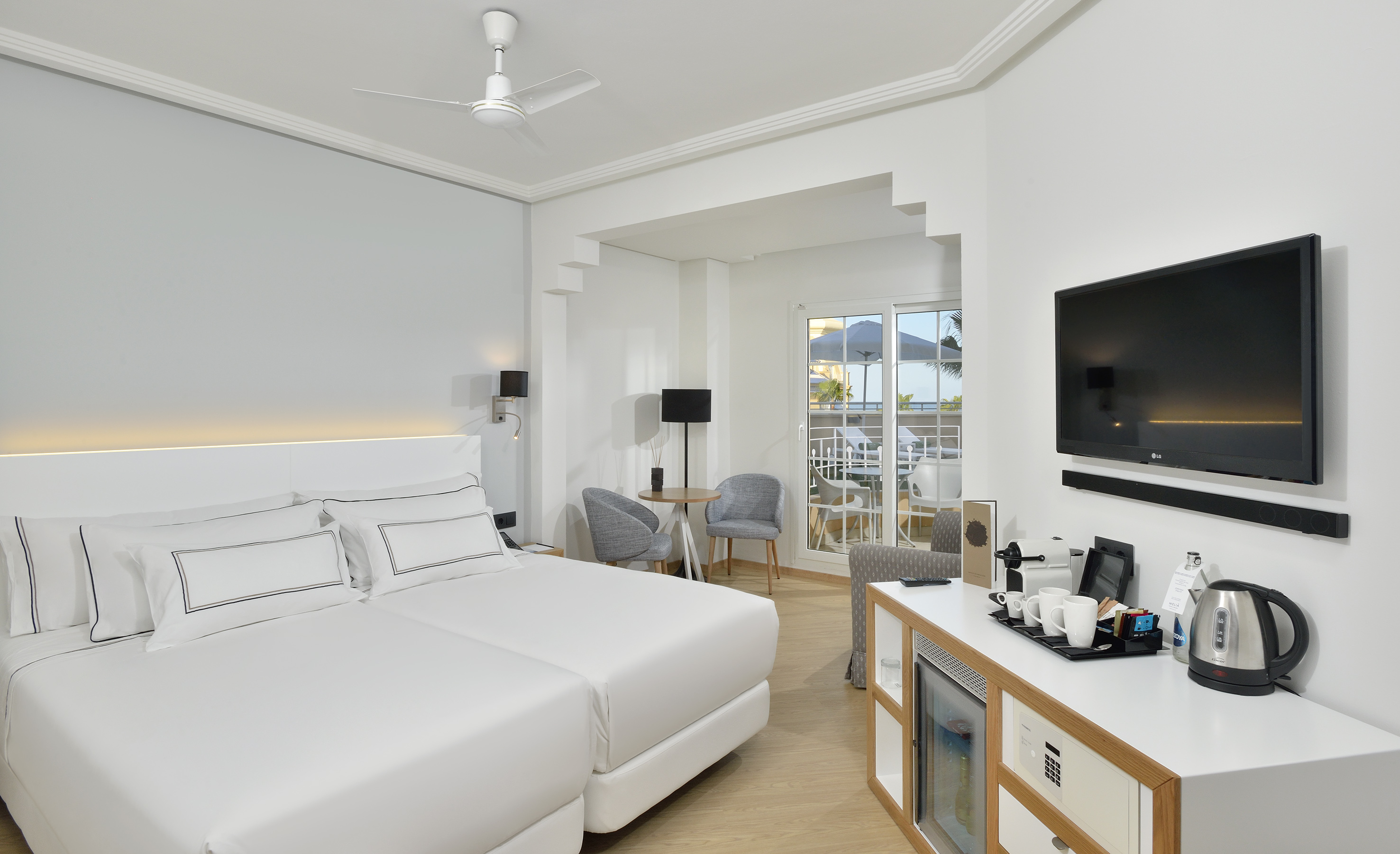 Modern hotel guest room with two beds, balcony, TV, and coffee amenities.