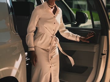 a woman in a white dress and sunglasses walking out of a car