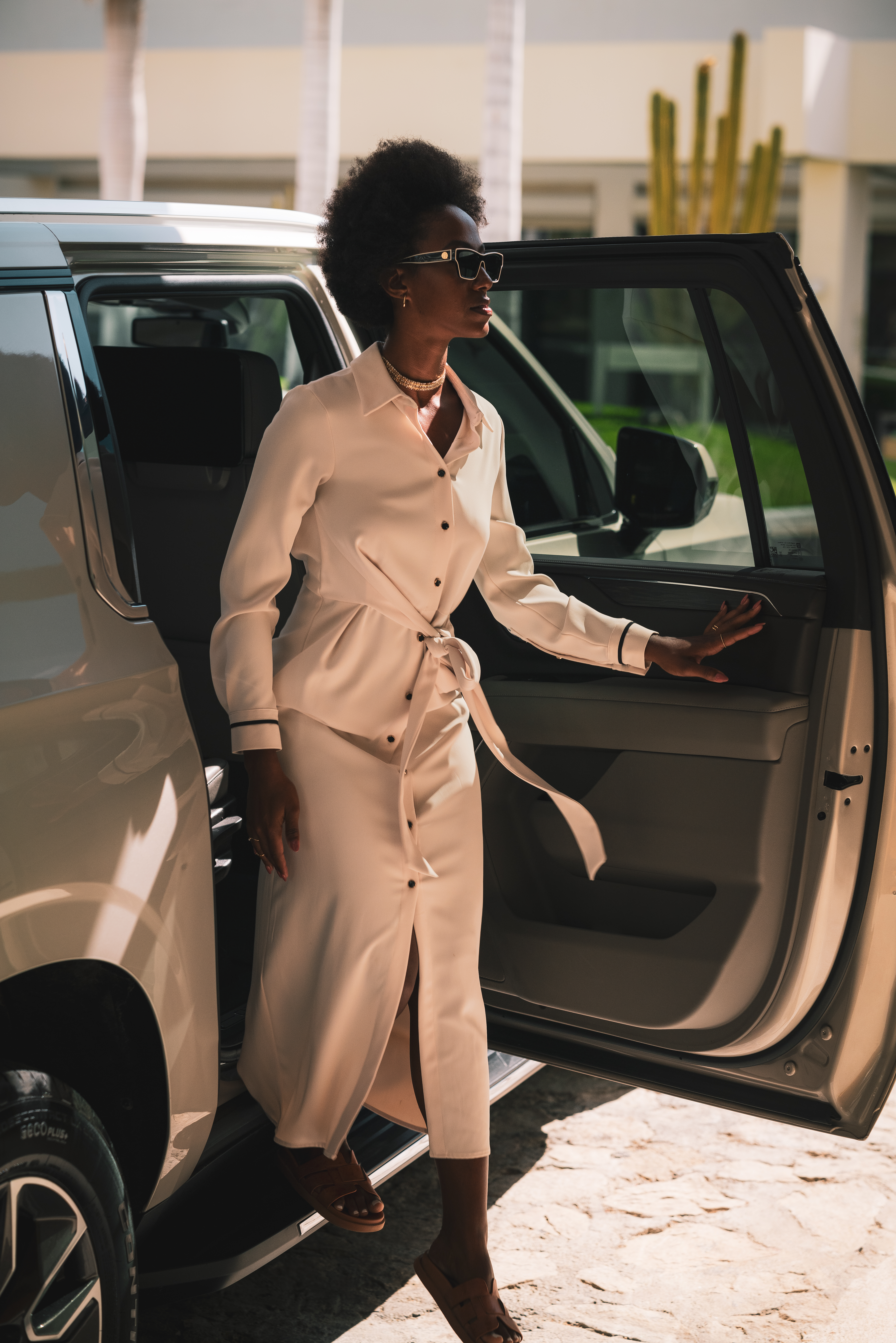 a woman in a white dress and sunglasses walking out of a car