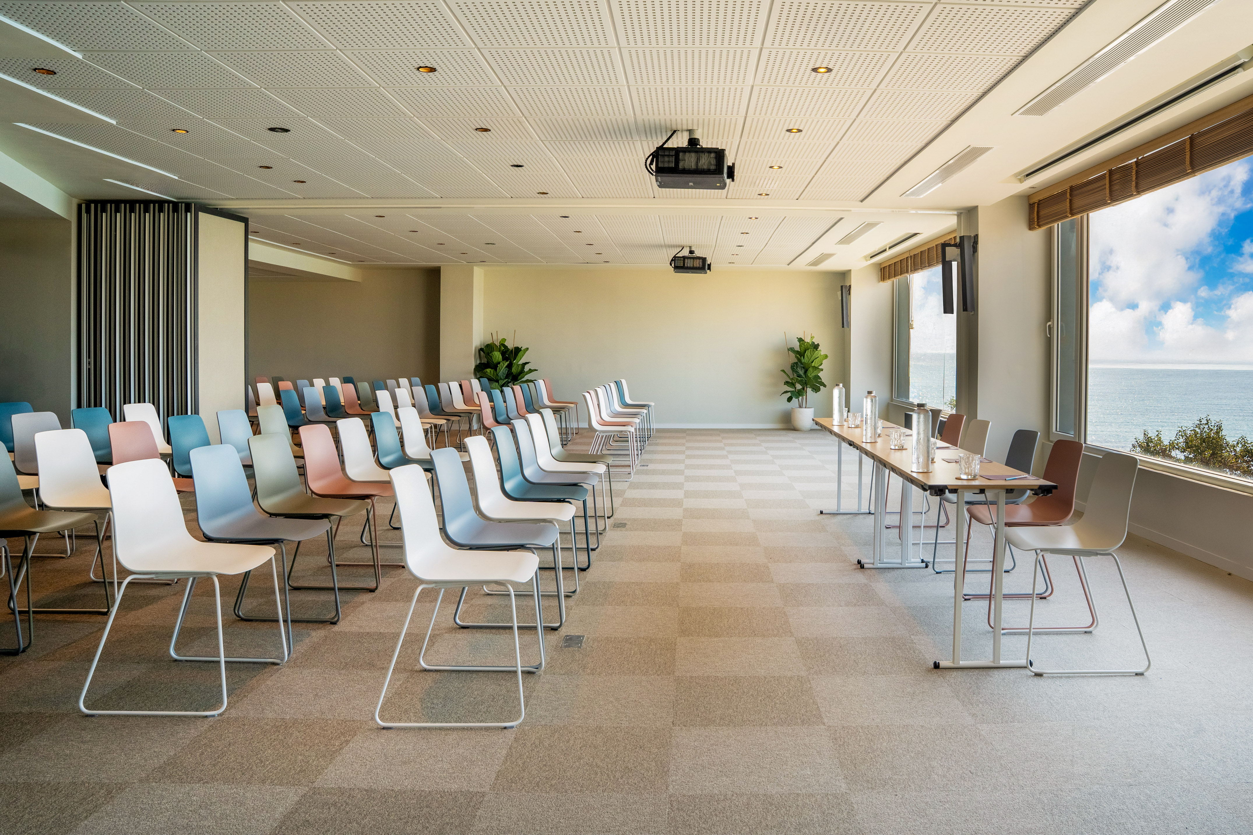 Bright conference room with colorful chairs, projector, and ocean view.