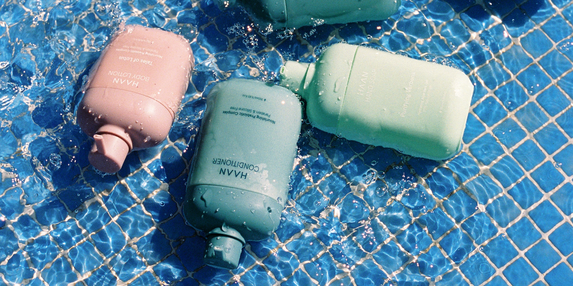 HAAN shampoo, conditioner, body wash, lotion bottles in blue pool.
