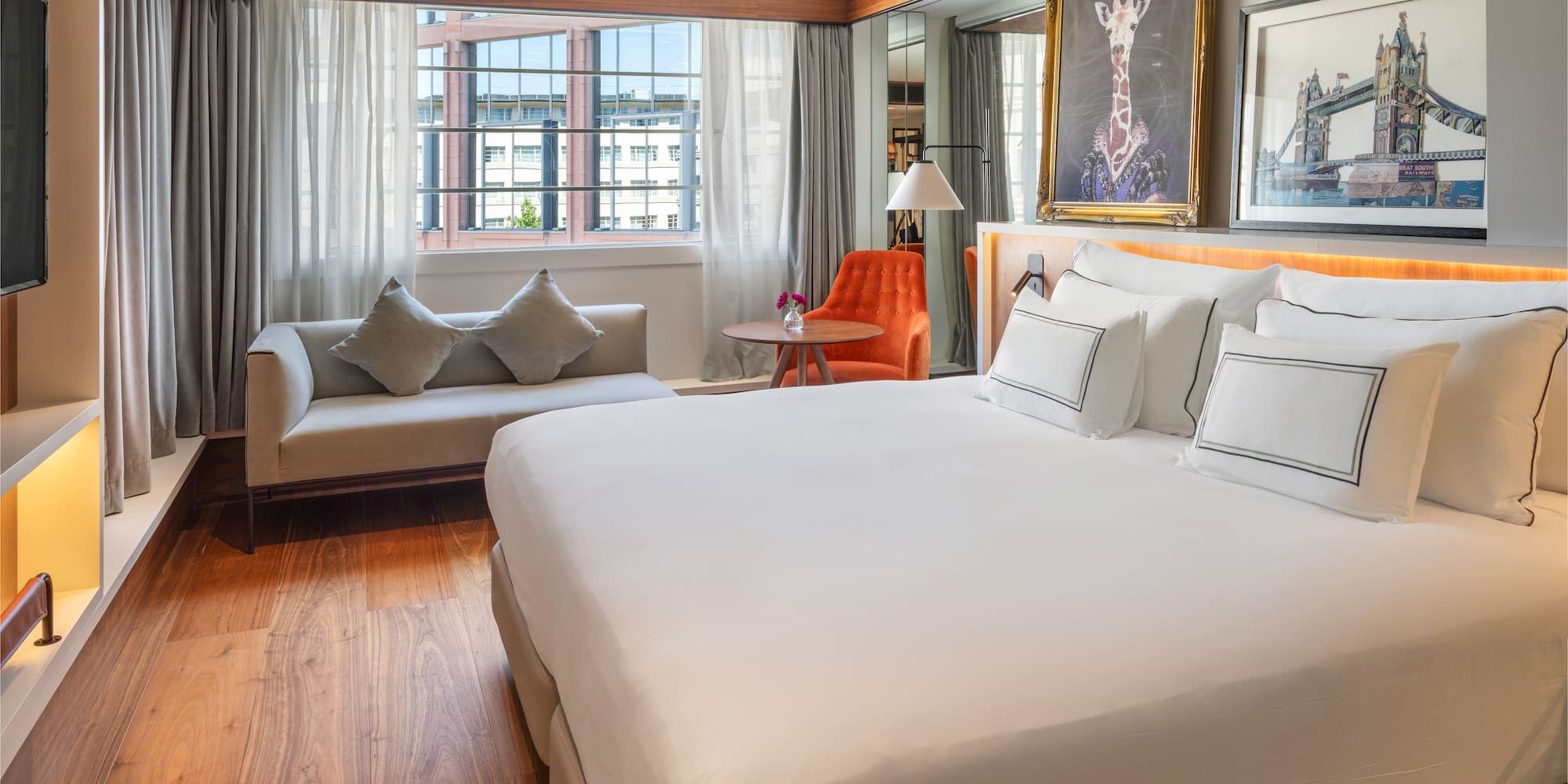 Luxury hotel bedroom with king bed, sofa, city view, and decorative art.