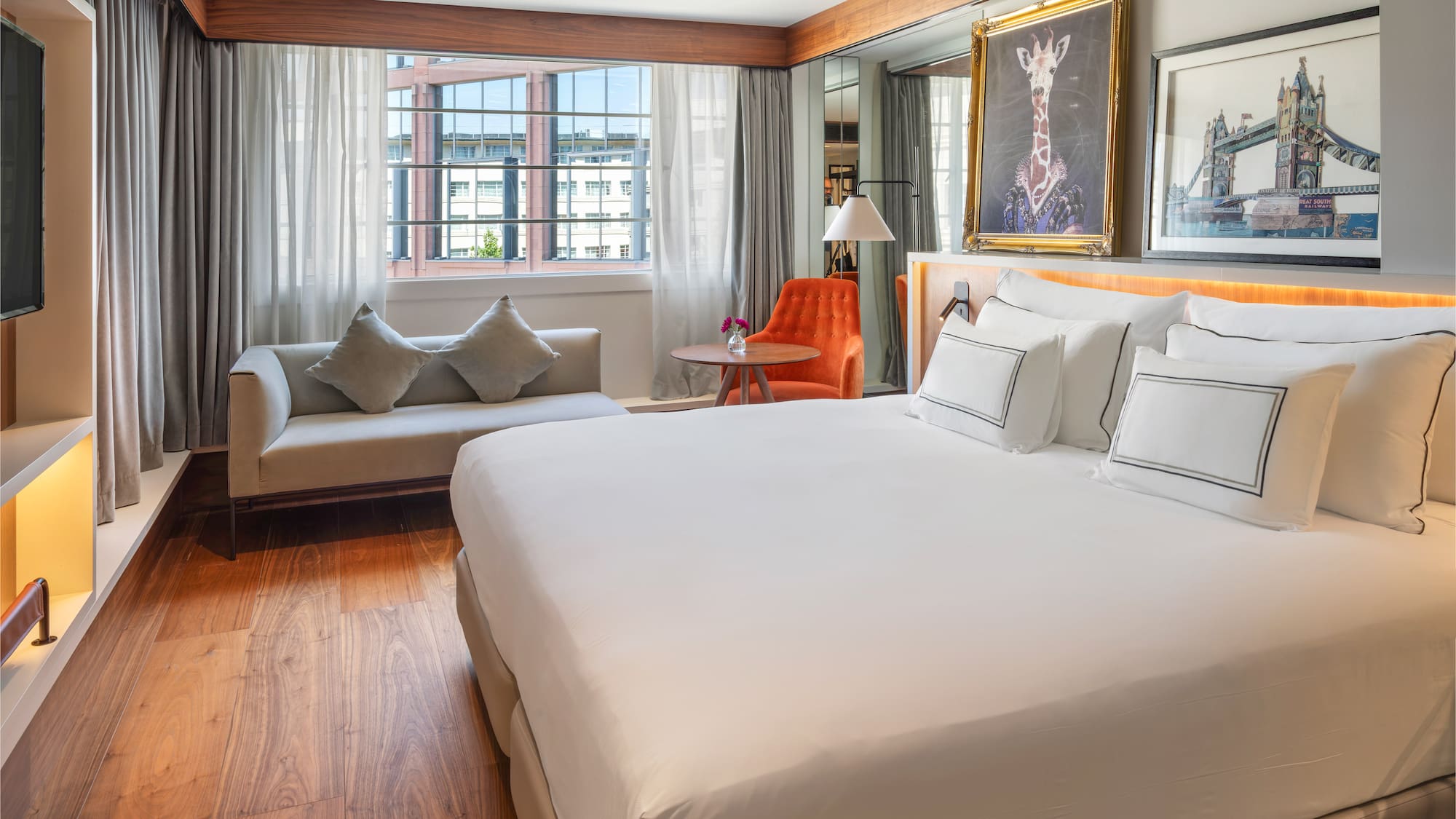 Luxury hotel bedroom with king bed, sofa, city view, and decorative art.