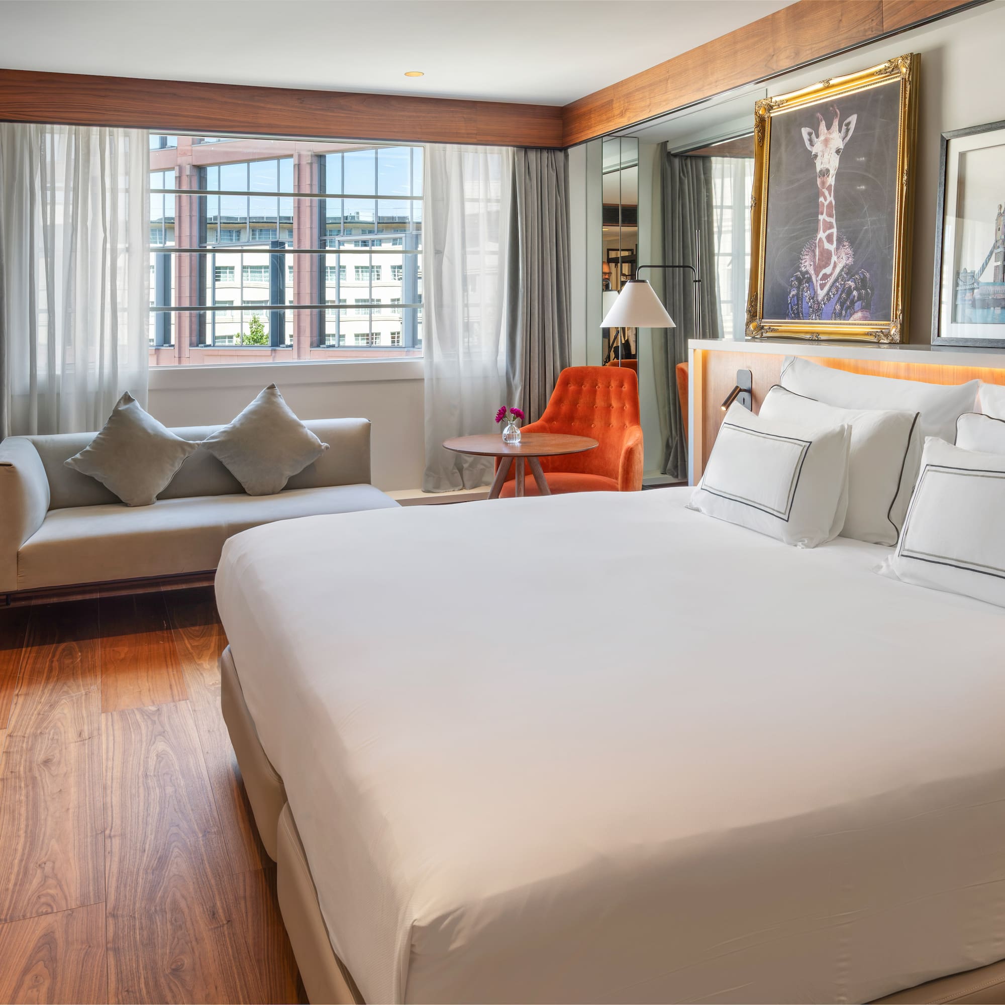 Luxury hotel bedroom with king bed, sofa, city view, and decorative art.