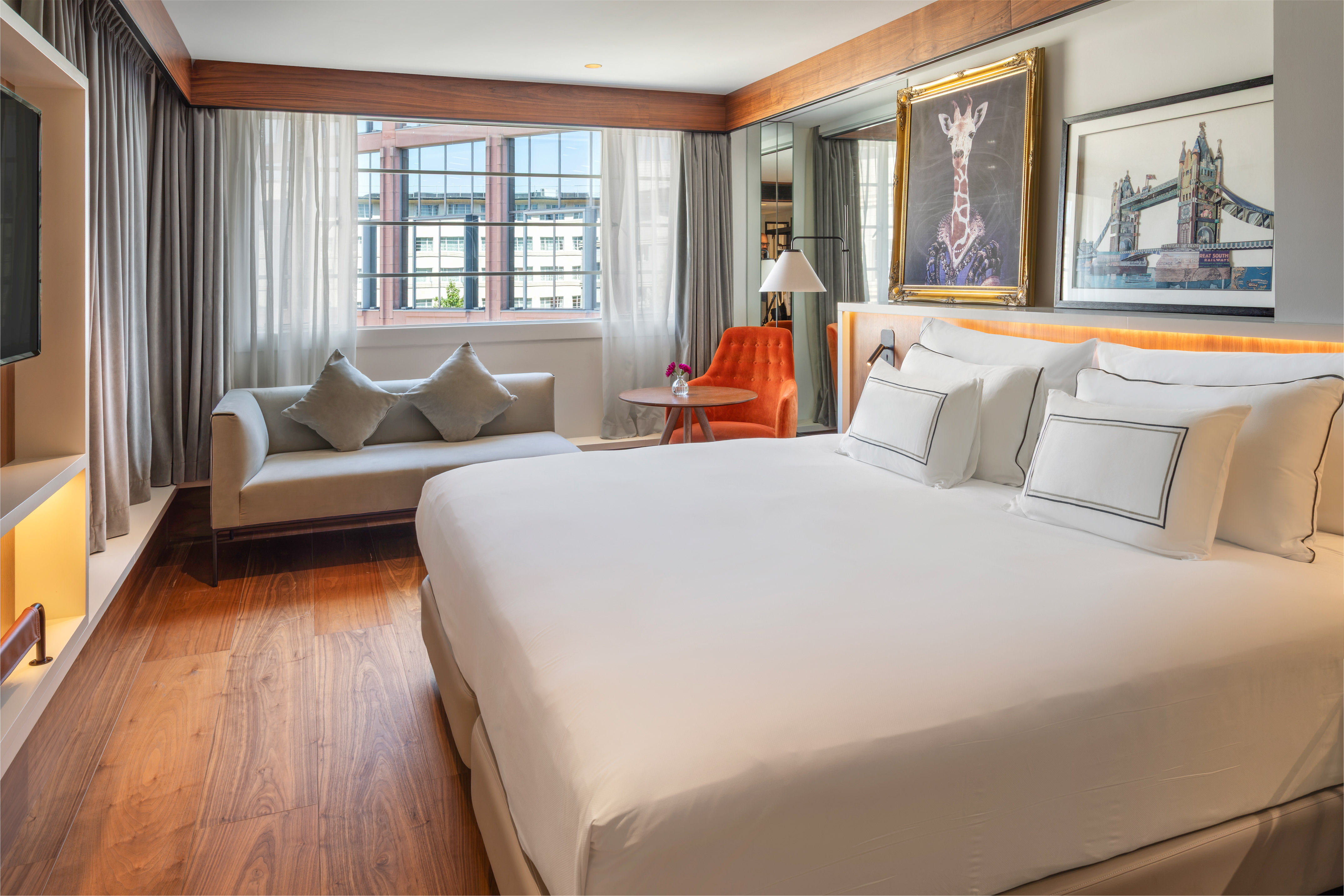 Luxury hotel bedroom with king bed, sofa, city view, and decorative art.