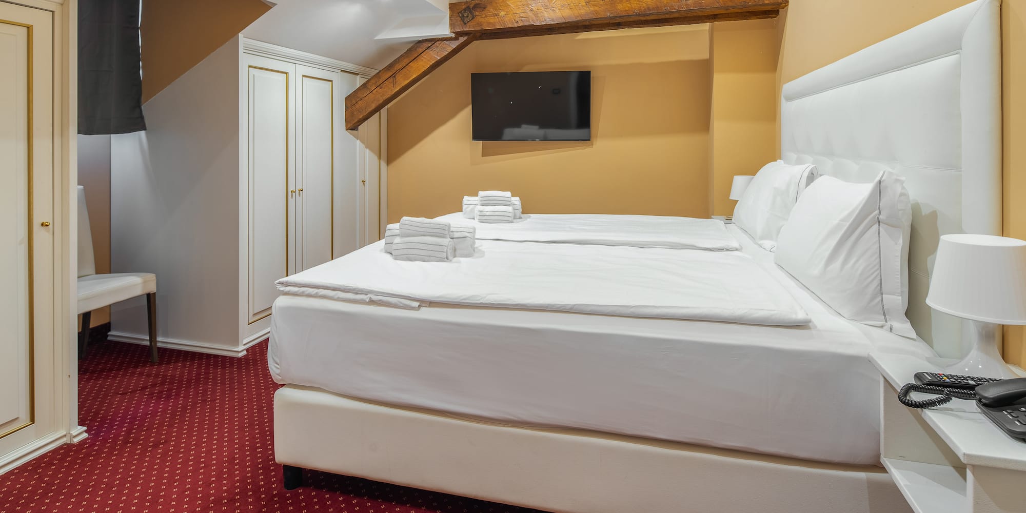 Cozy hotel bedroom with twin beds, white linens, red carpet, and exposed beams.