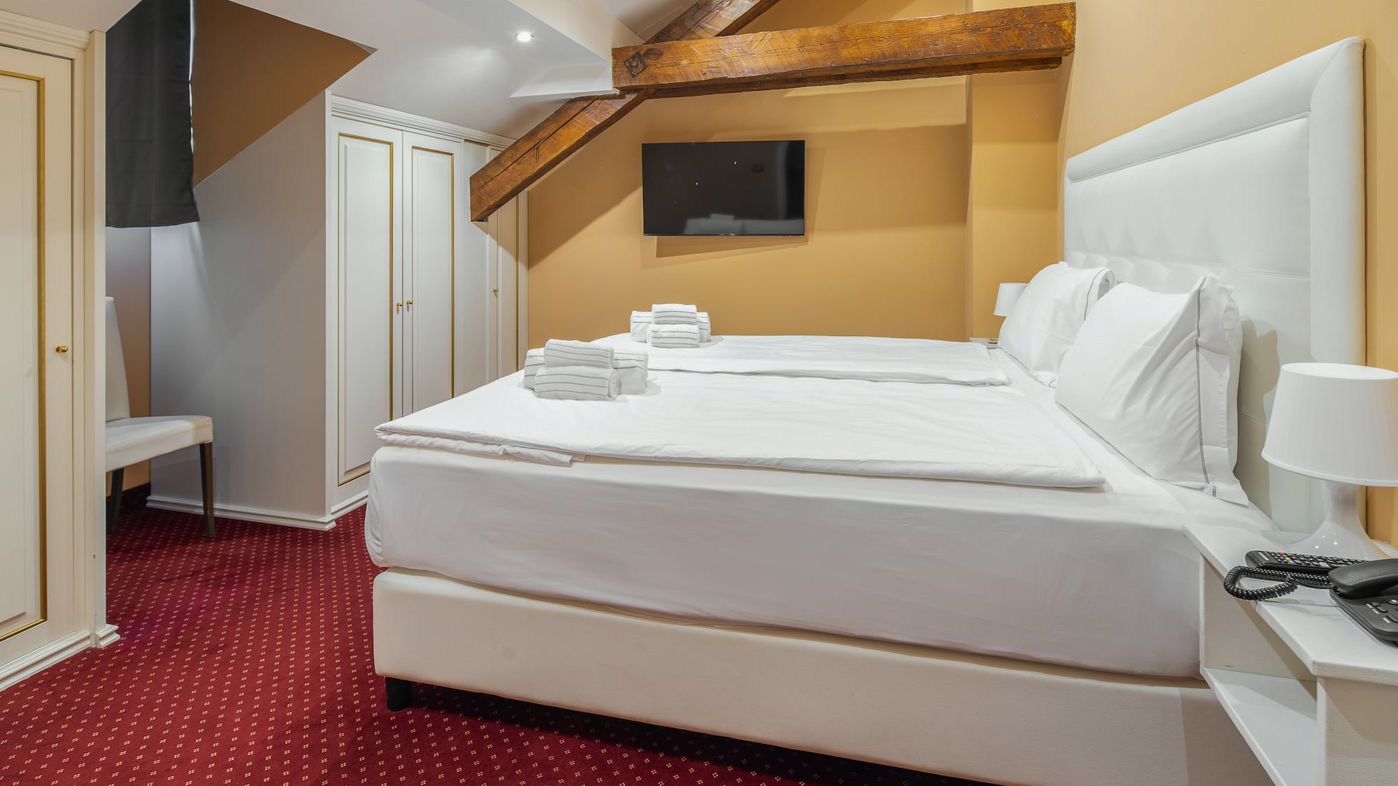 Cozy hotel bedroom with twin beds, white linens, red carpet, and exposed beams.