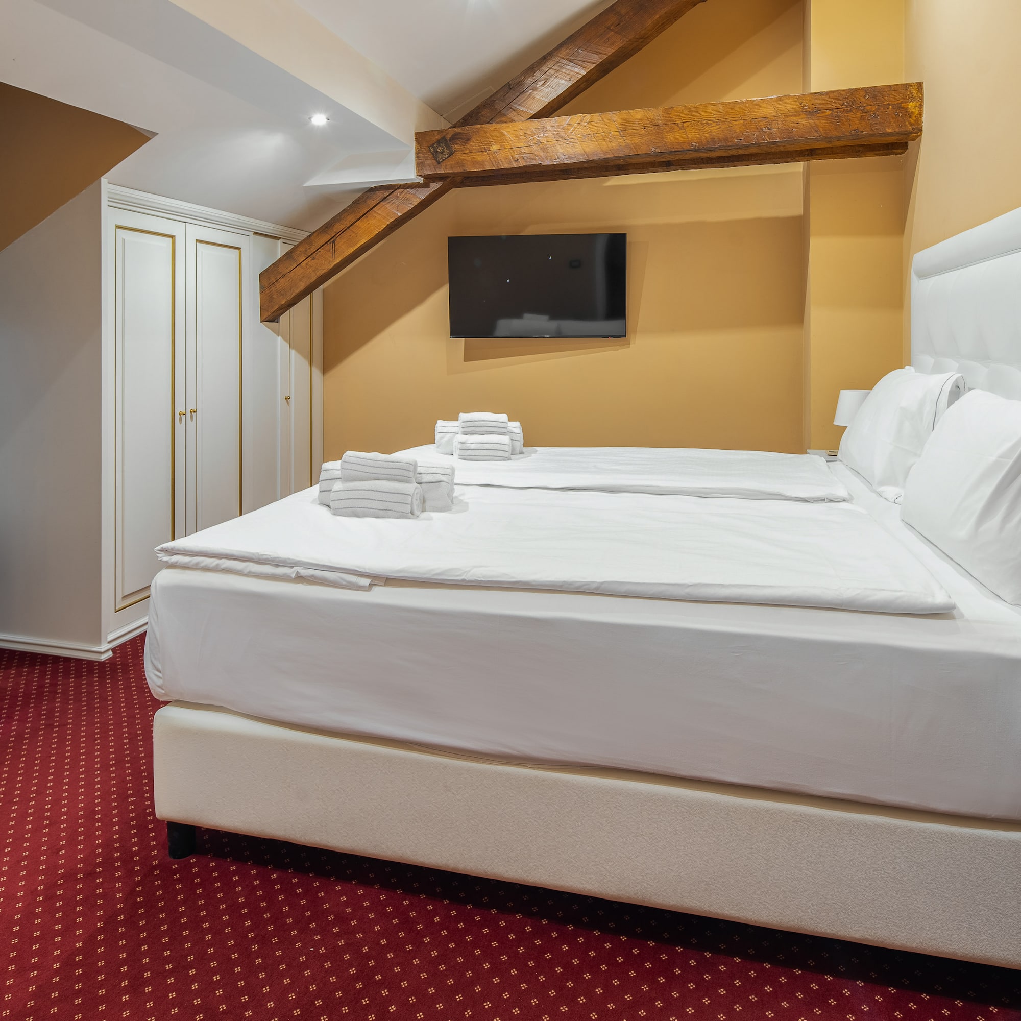 Cozy hotel bedroom with twin beds, white linens, red carpet, and exposed beams.