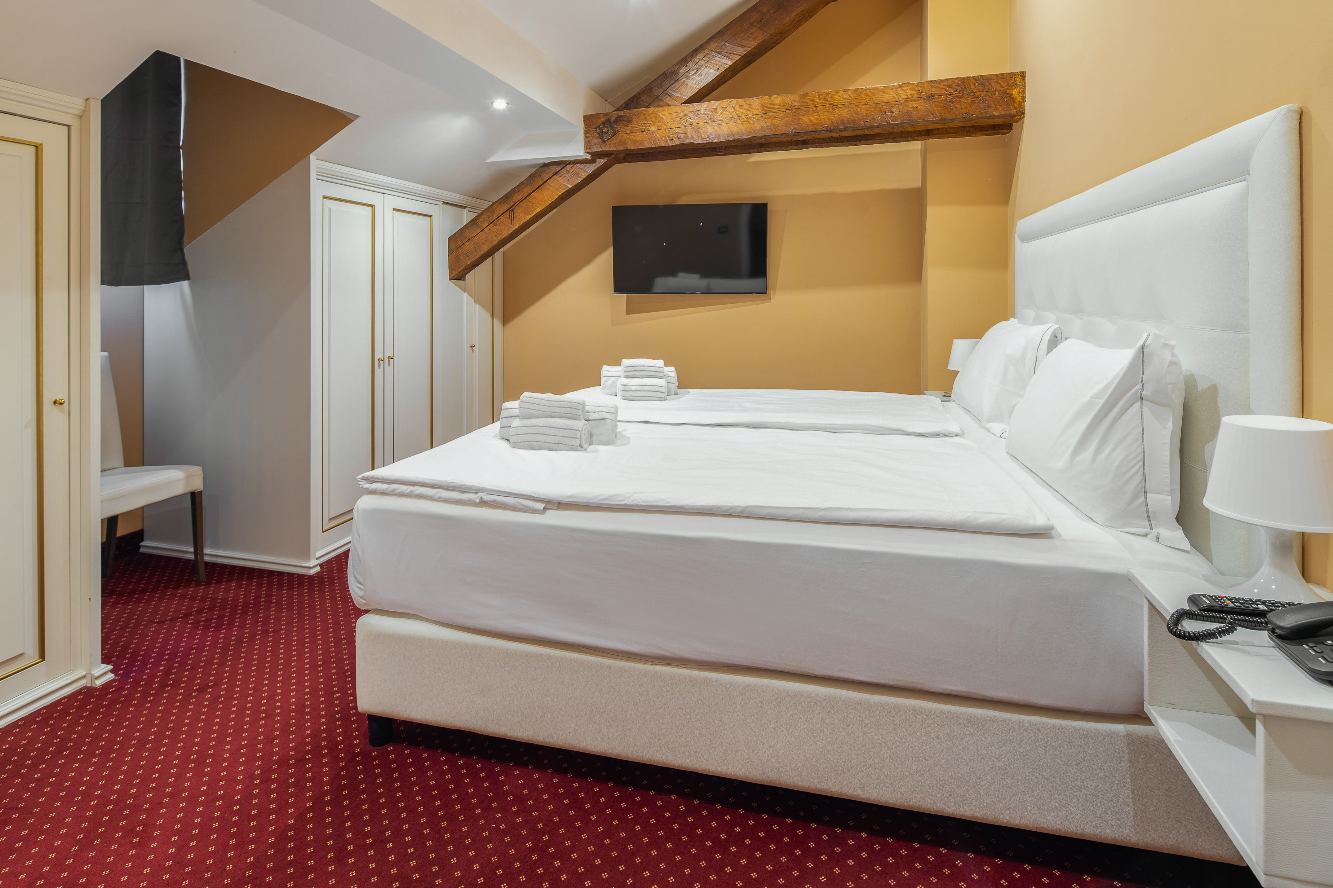 Cozy hotel bedroom with twin beds, white linens, red carpet, and exposed beams.