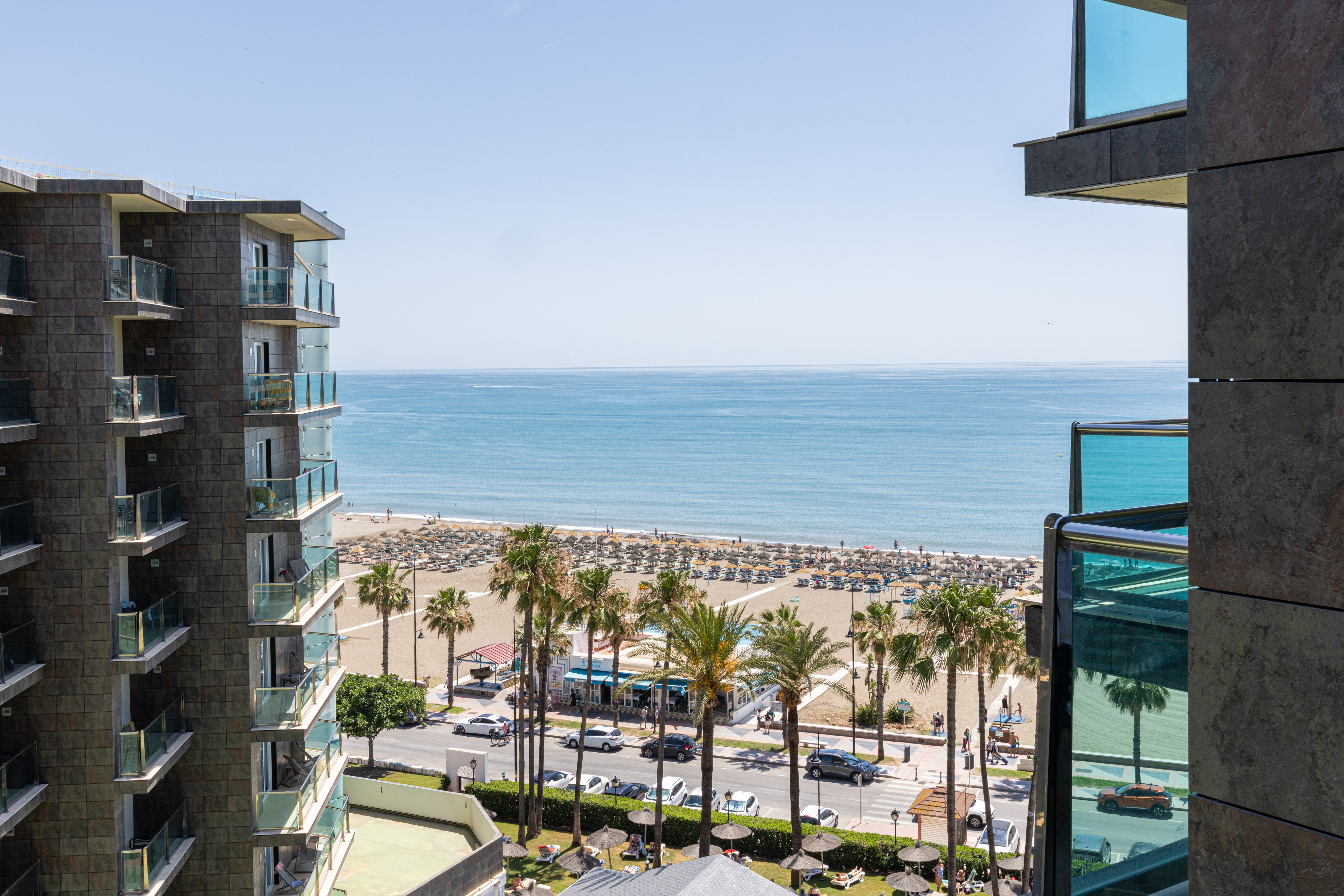 Sunny beach and ocean view from modern hotel balconies with palm trees.