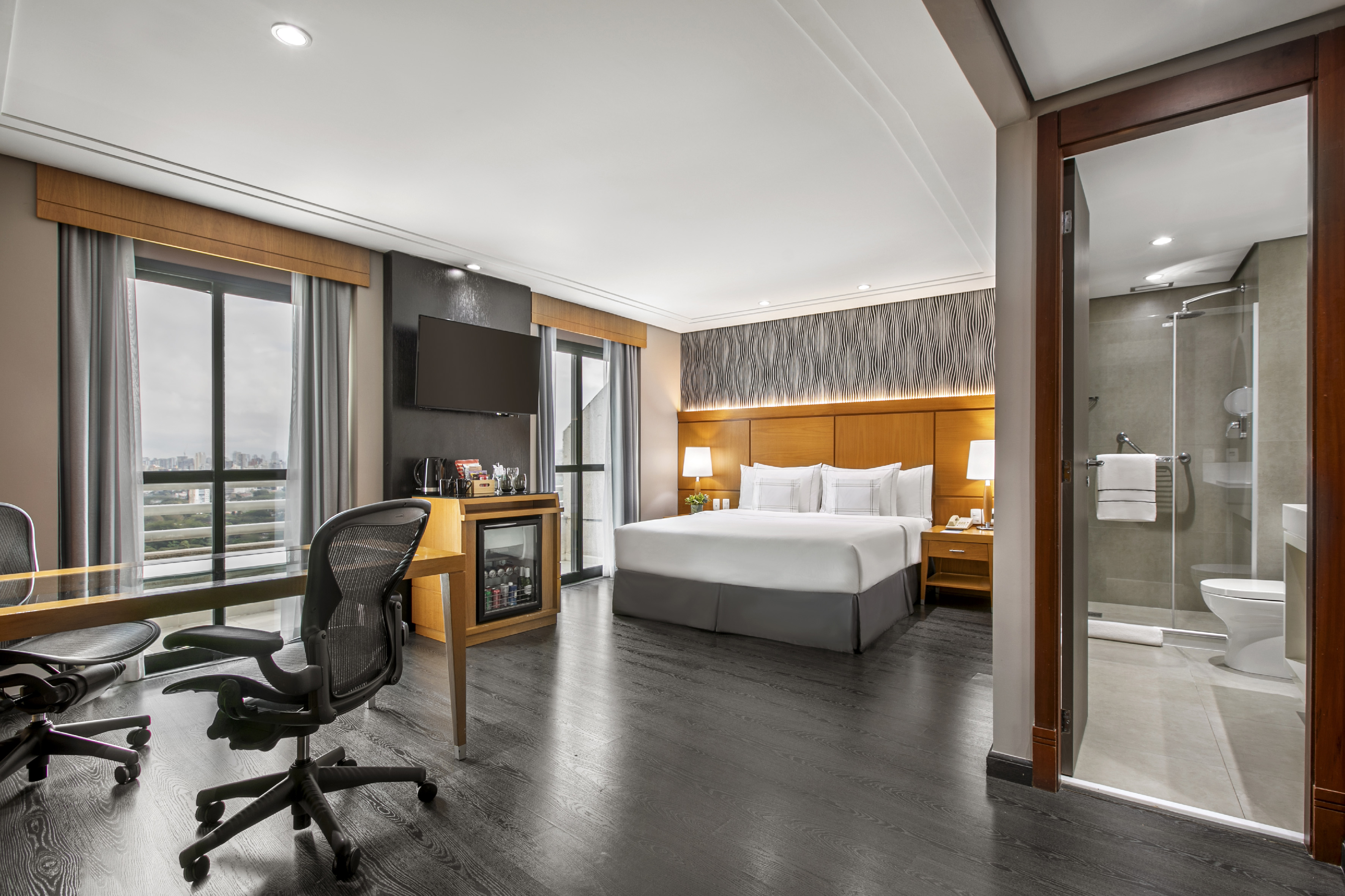 Modern hotel room with king bed, desk, city view, and ensuite bathroom.