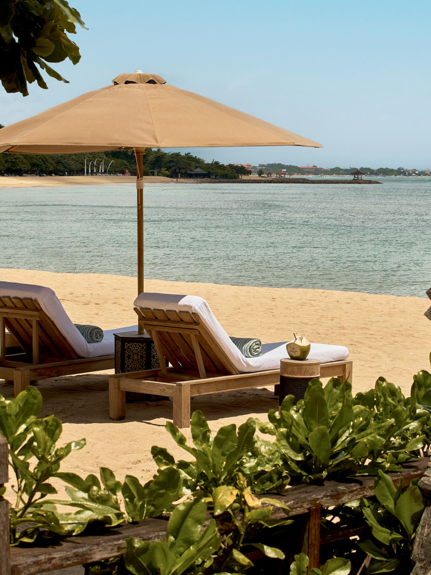Tropical resort beach with lounge chairs, umbrella, ocean, and Balinese statue.