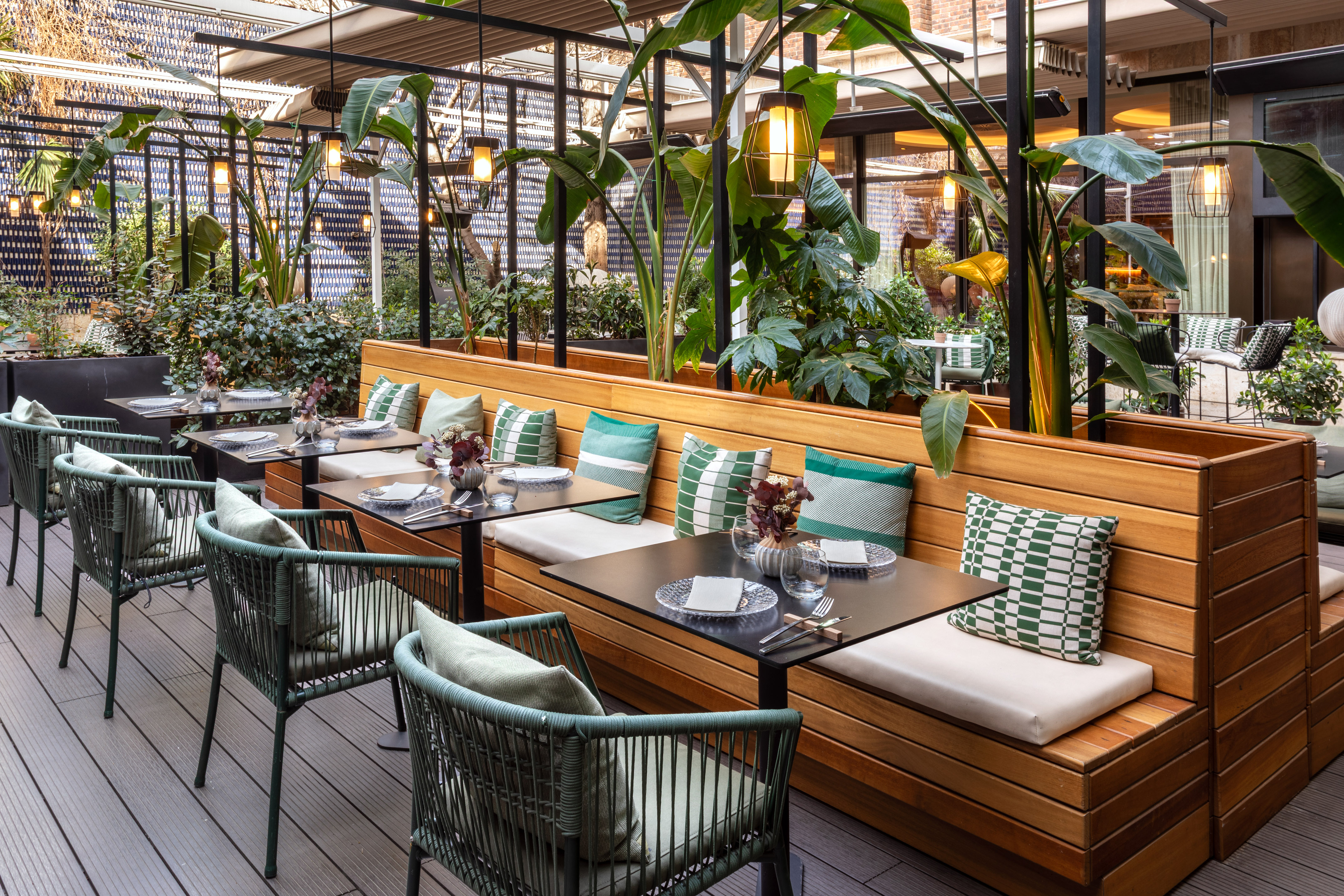 Stylish outdoor restaurant patio with wooden seating, green accents, and plants.