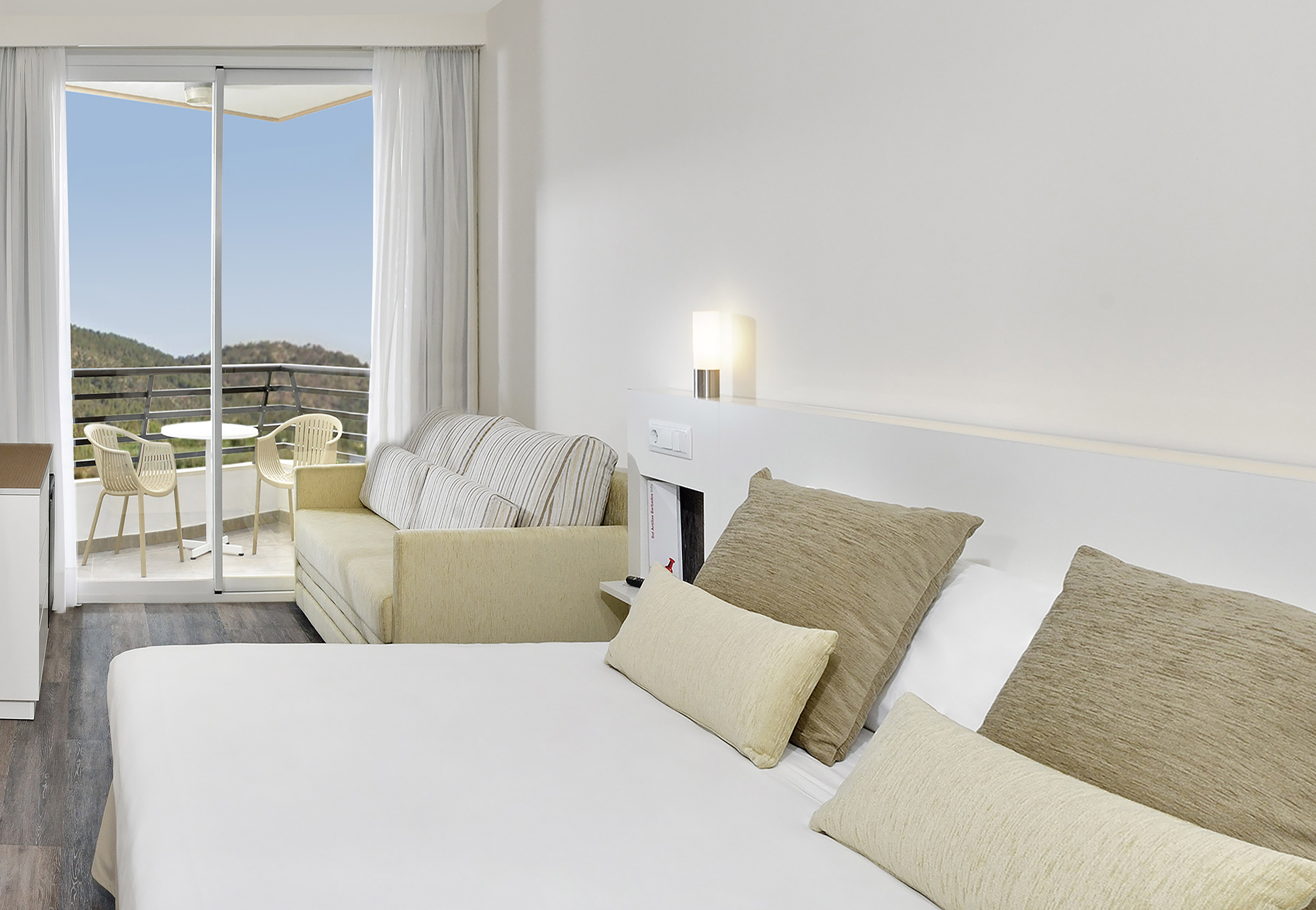 Modern resort room with bed, sofa, and private balcony overlooking mountains.