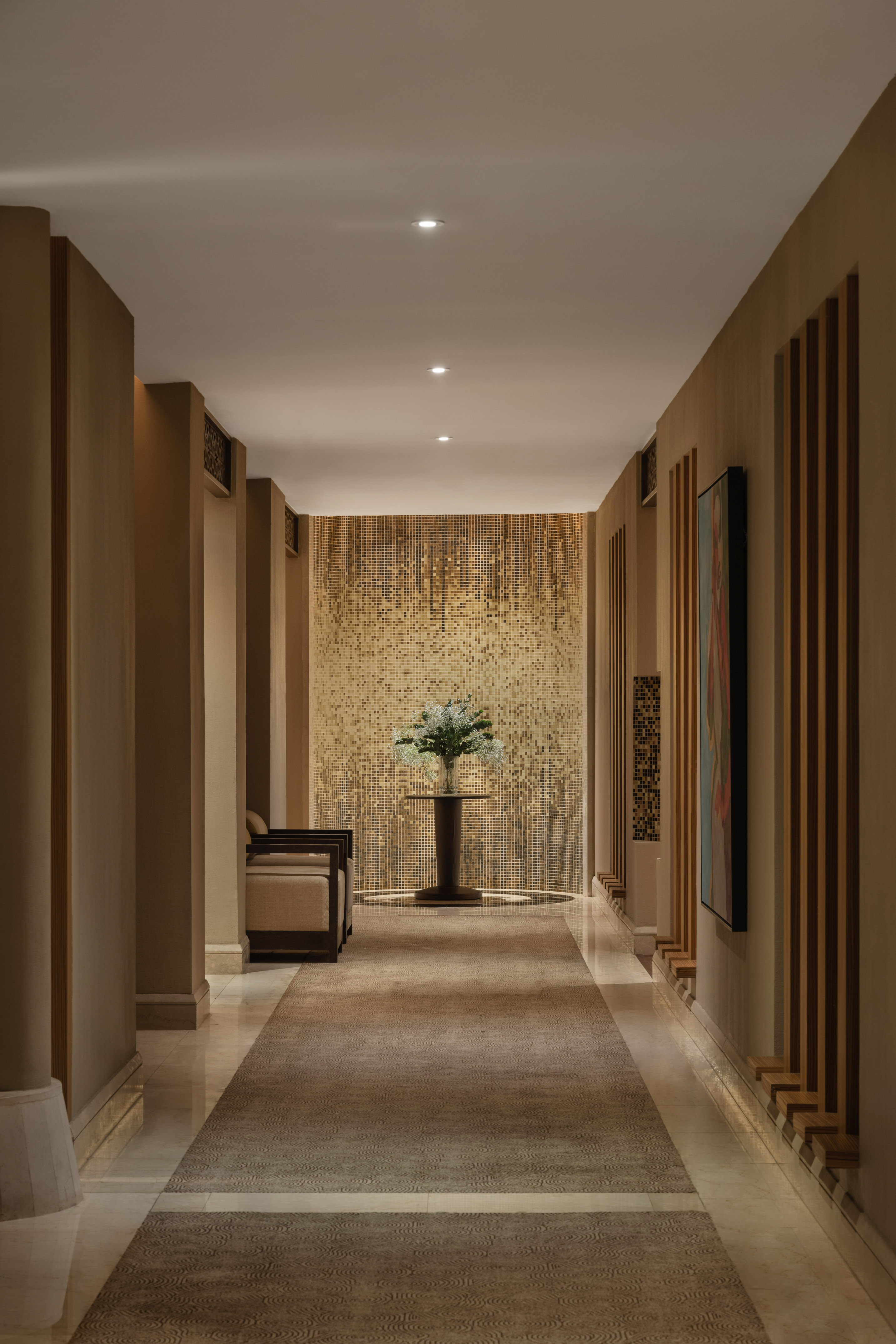 Hotel hallway with golden mosaic wall, floral centerpiece, patterned rug.