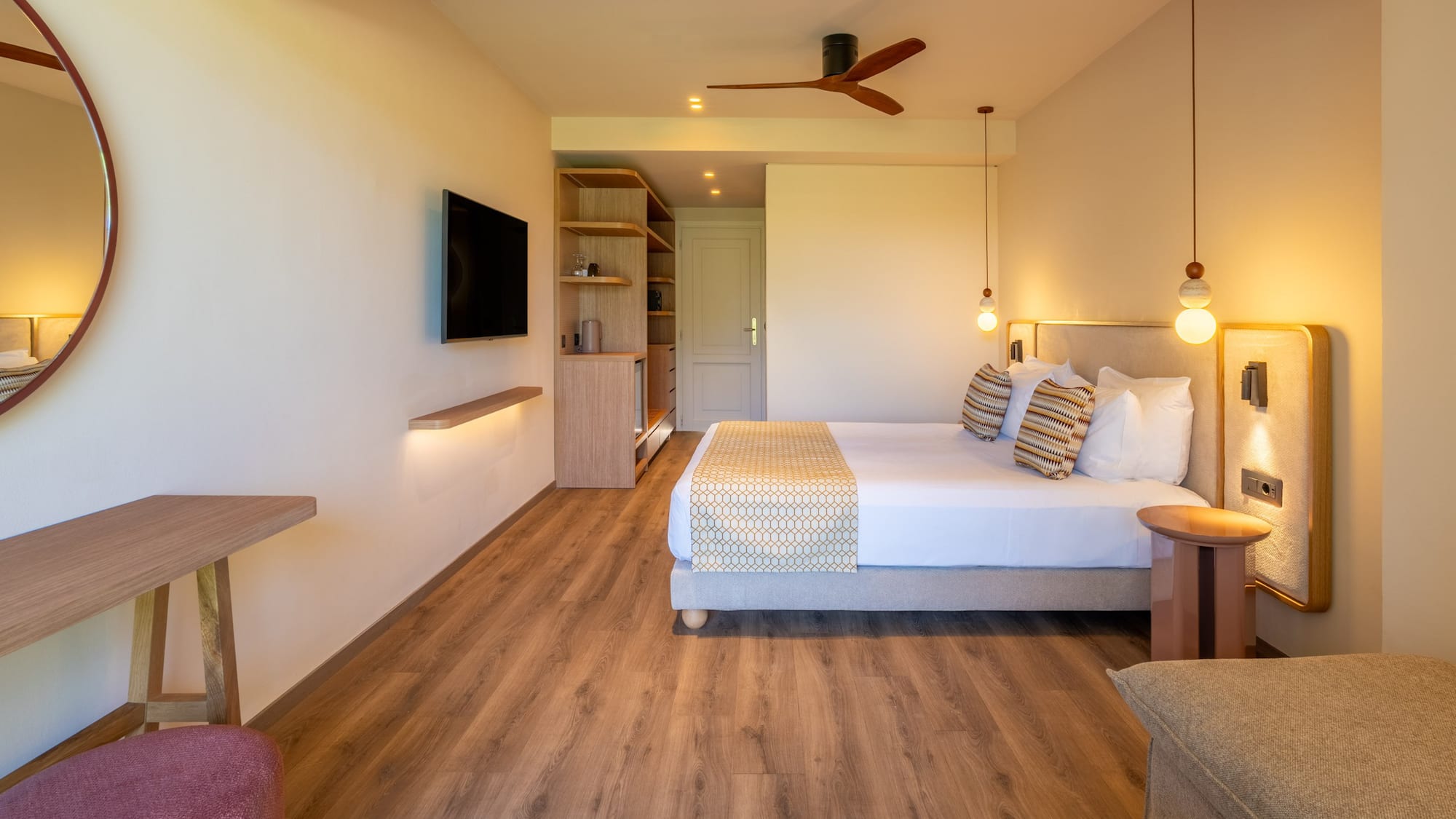 Contemporary hotel bedroom with large bed, TV, wooden floor, ceiling fan.