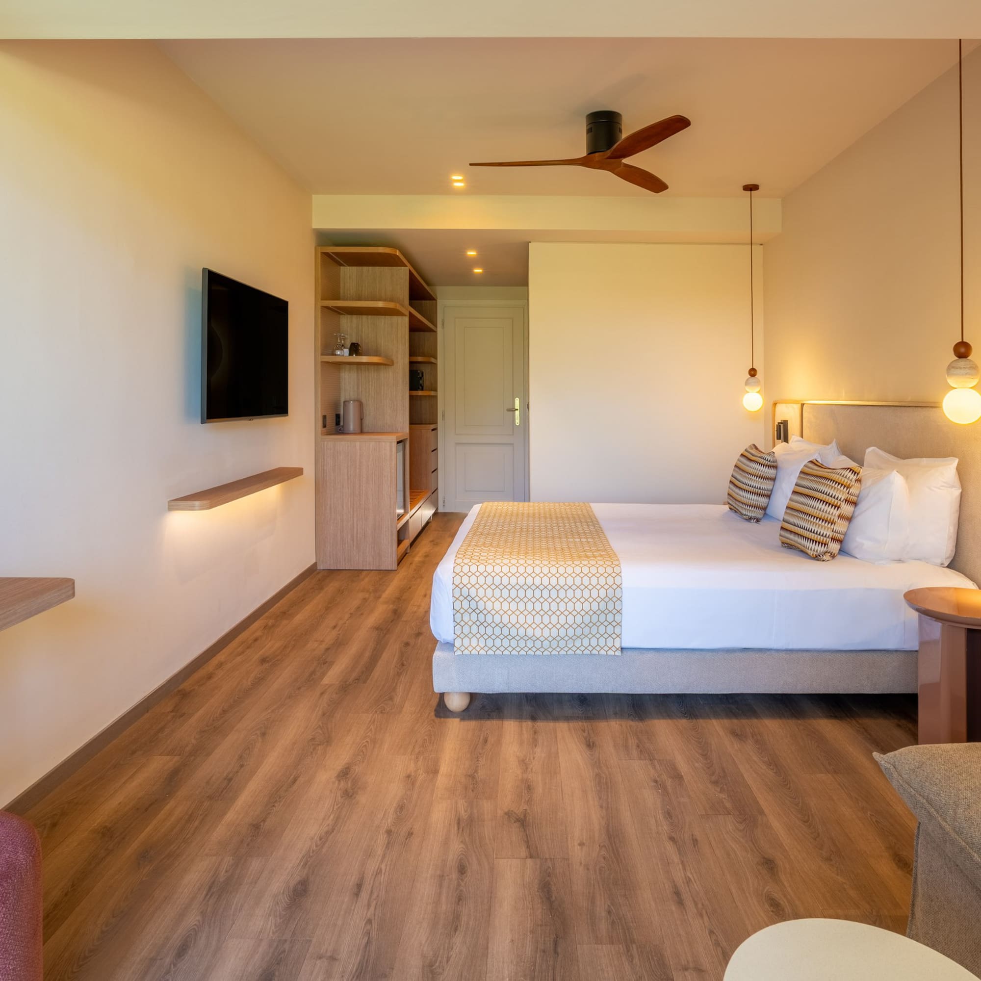 Contemporary hotel bedroom with large bed, TV, wooden floor, ceiling fan.