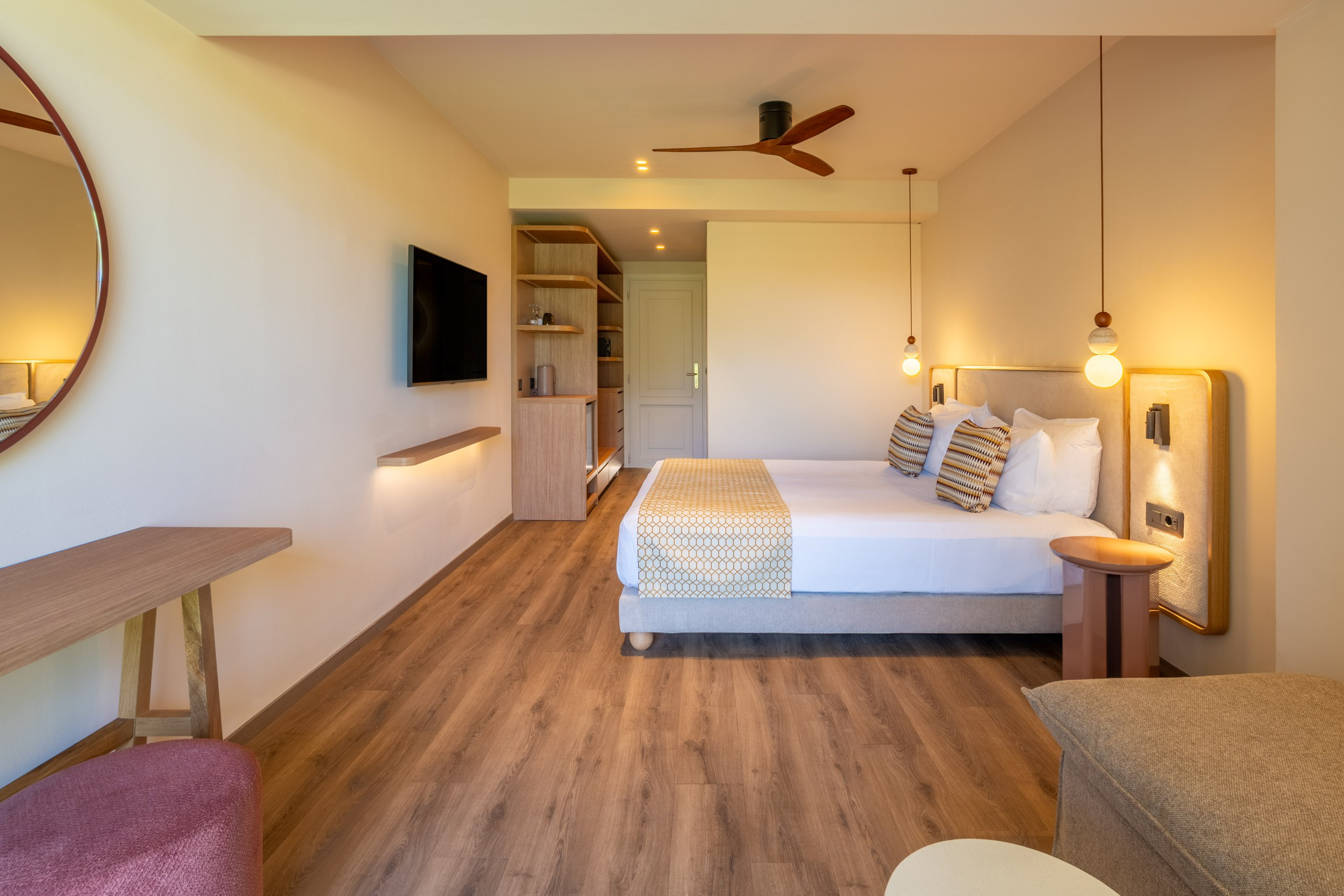 Contemporary hotel bedroom with large bed, TV, wooden floor, ceiling fan.