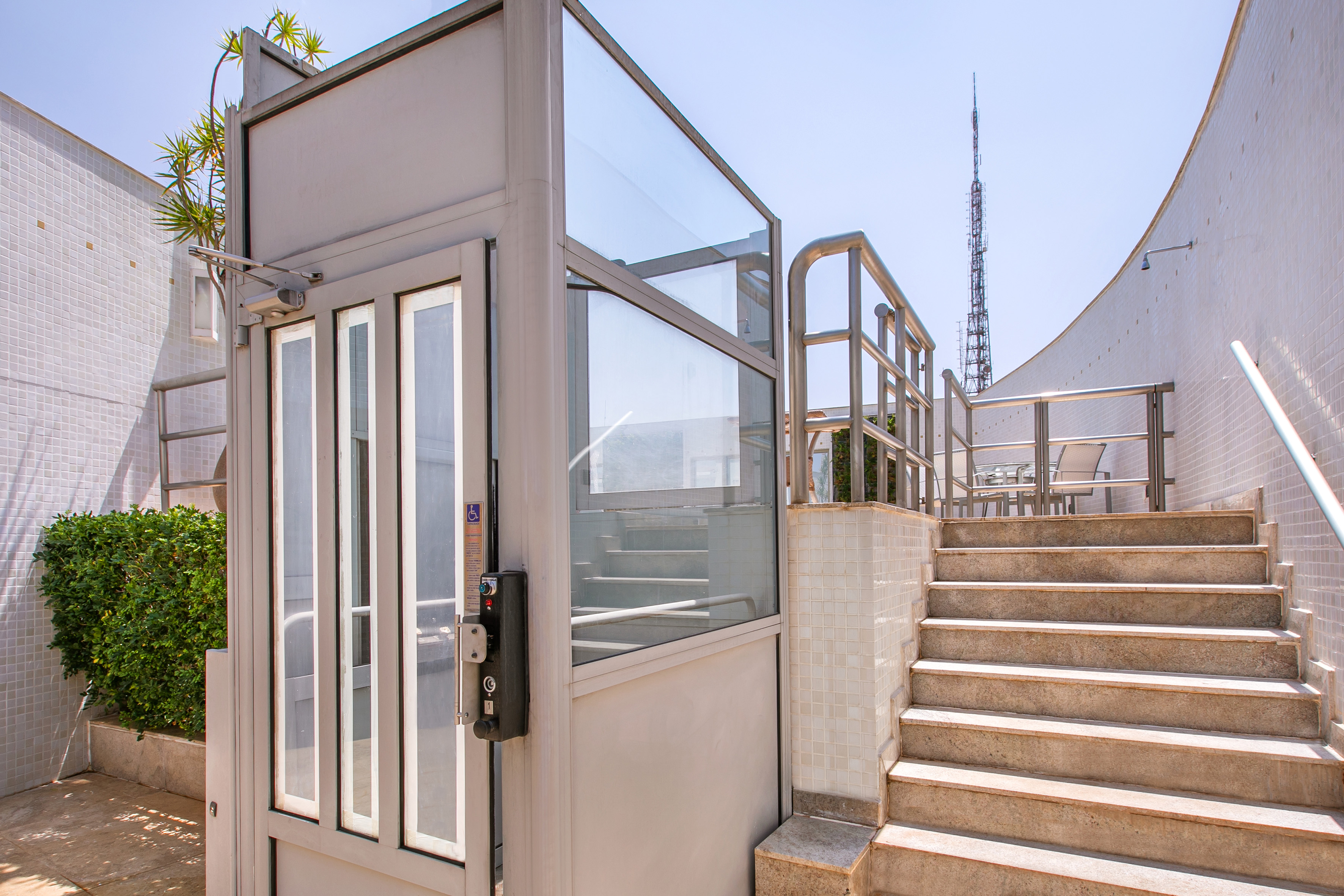 Outdoor wheelchair platform lift next to stairs with railing, building access.