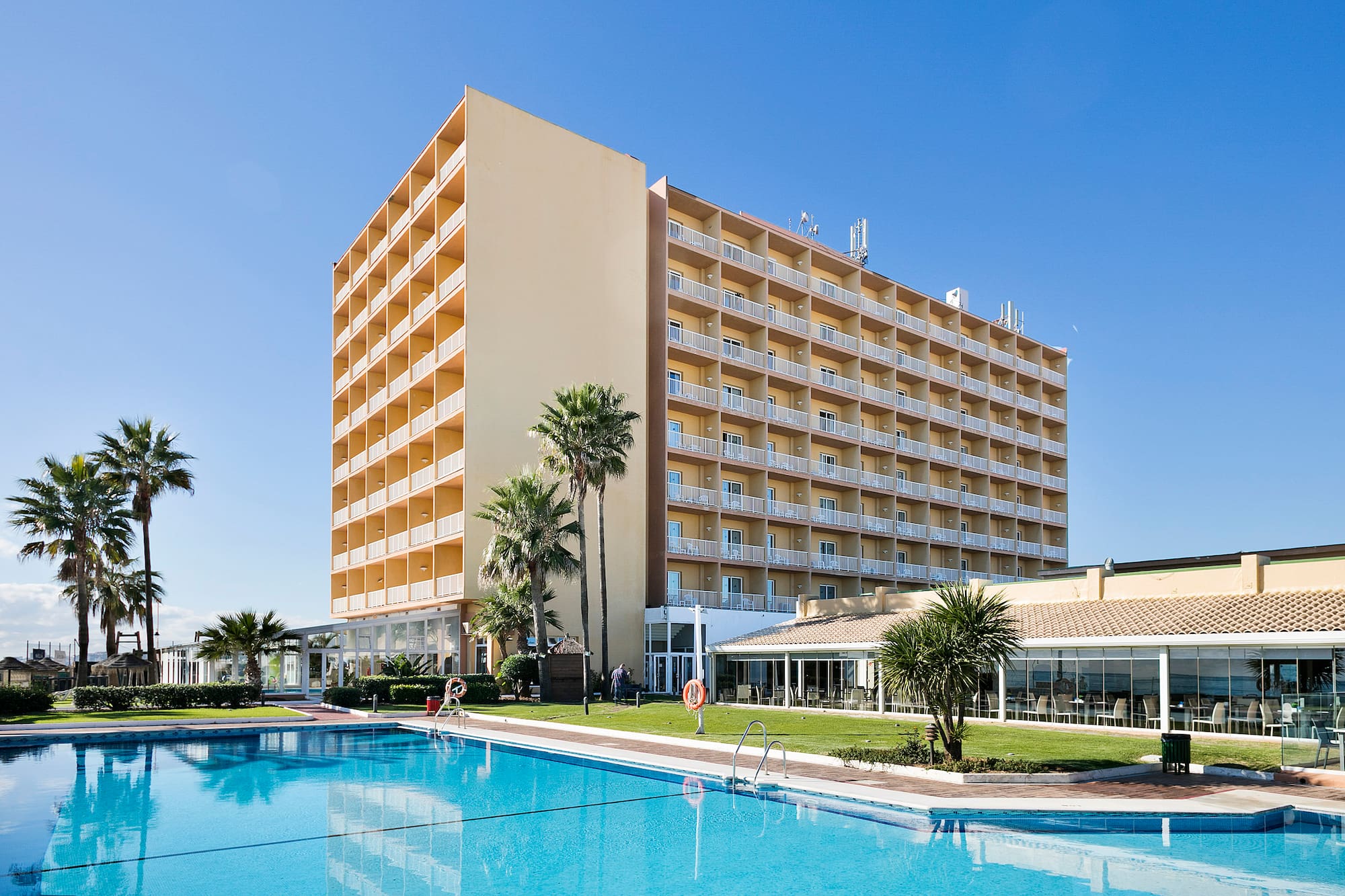 Hotel resort with large swimming pool, palm trees, and balconies.