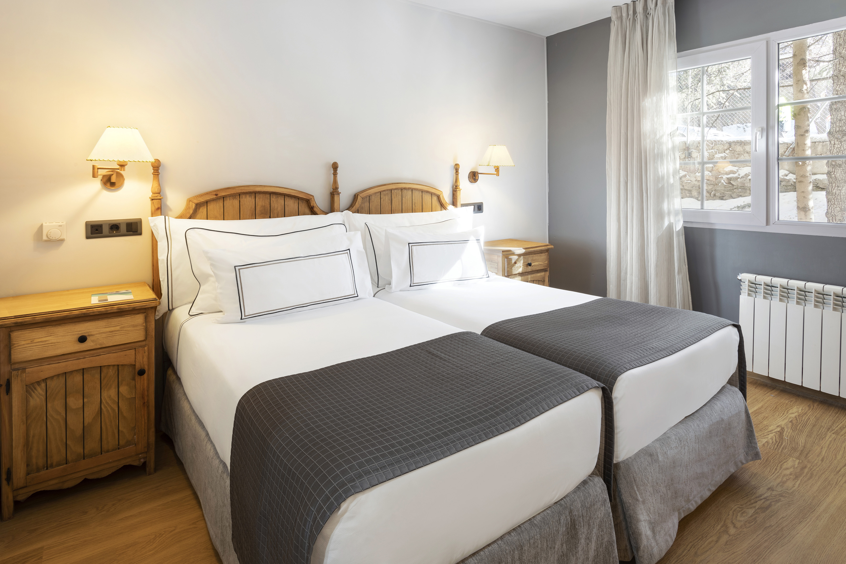 Hotel twin bedroom with wooden beds, nightstands, and window view.