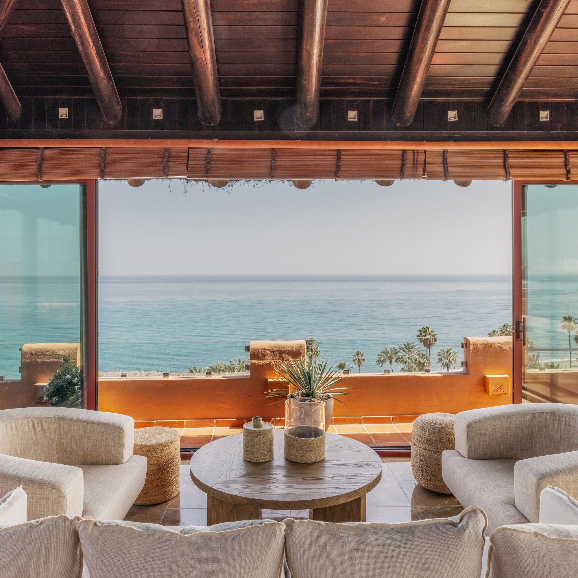 Bright living room with sea view, large glass windows, modern seating, wood ceiling.