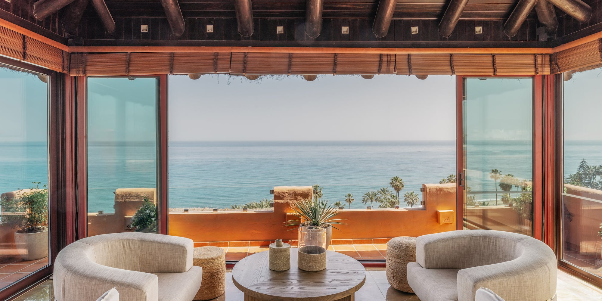 Bright living room with sea view, large glass windows, modern seating, wood ceiling.