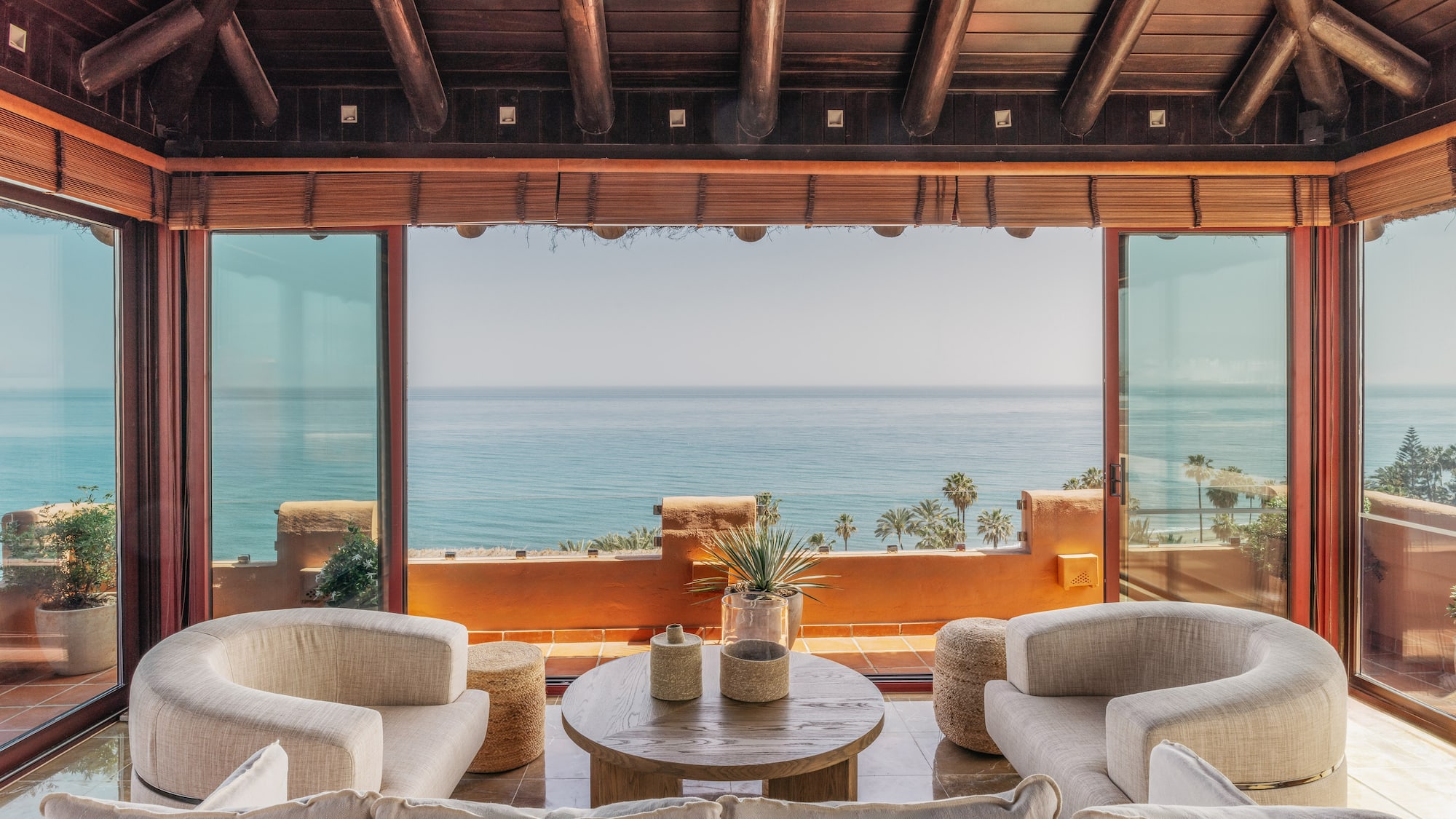 Bright living room with sea view, large glass windows, modern seating, wood ceiling.