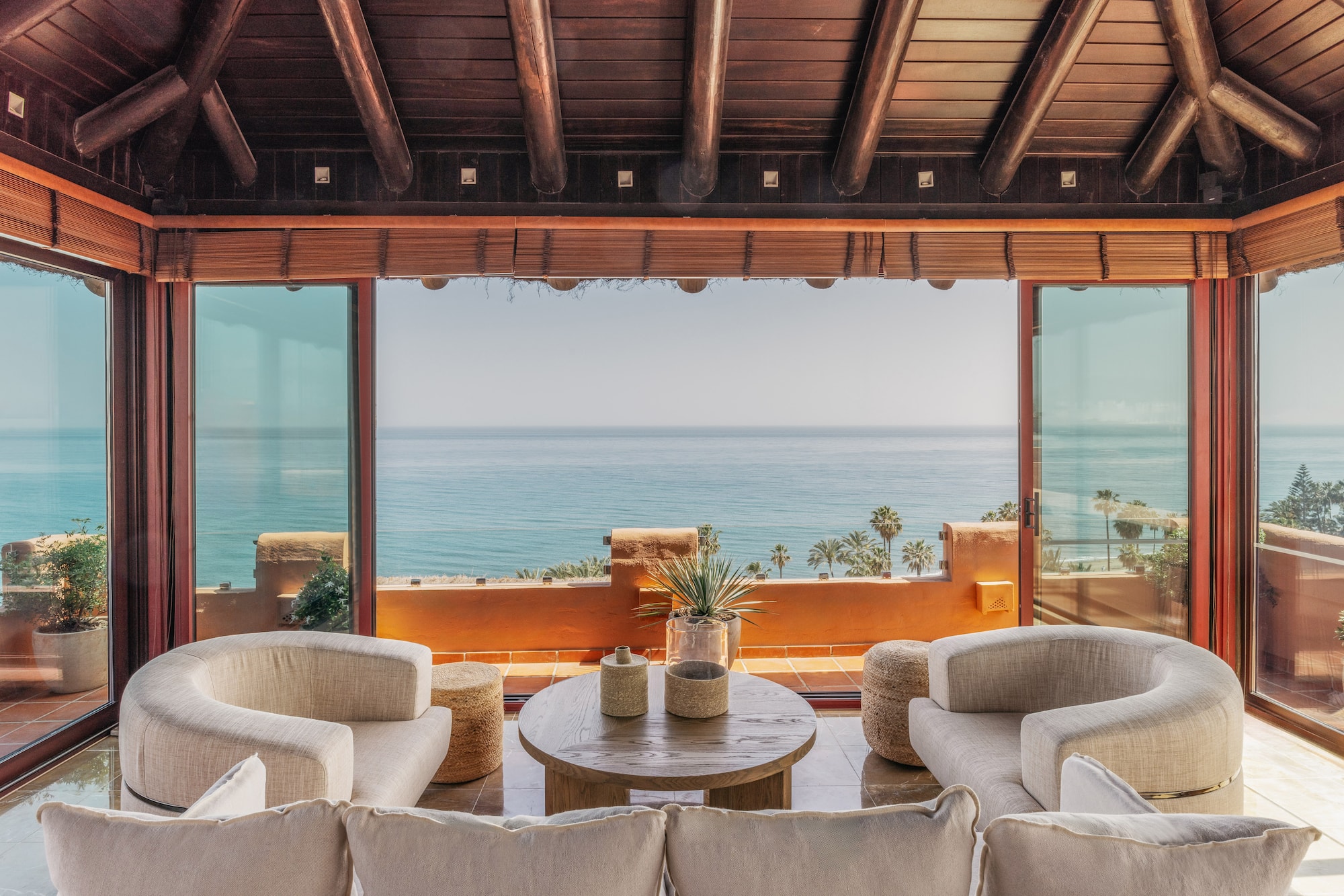 Bright living room with sea view, large glass windows, modern seating, wood ceiling.