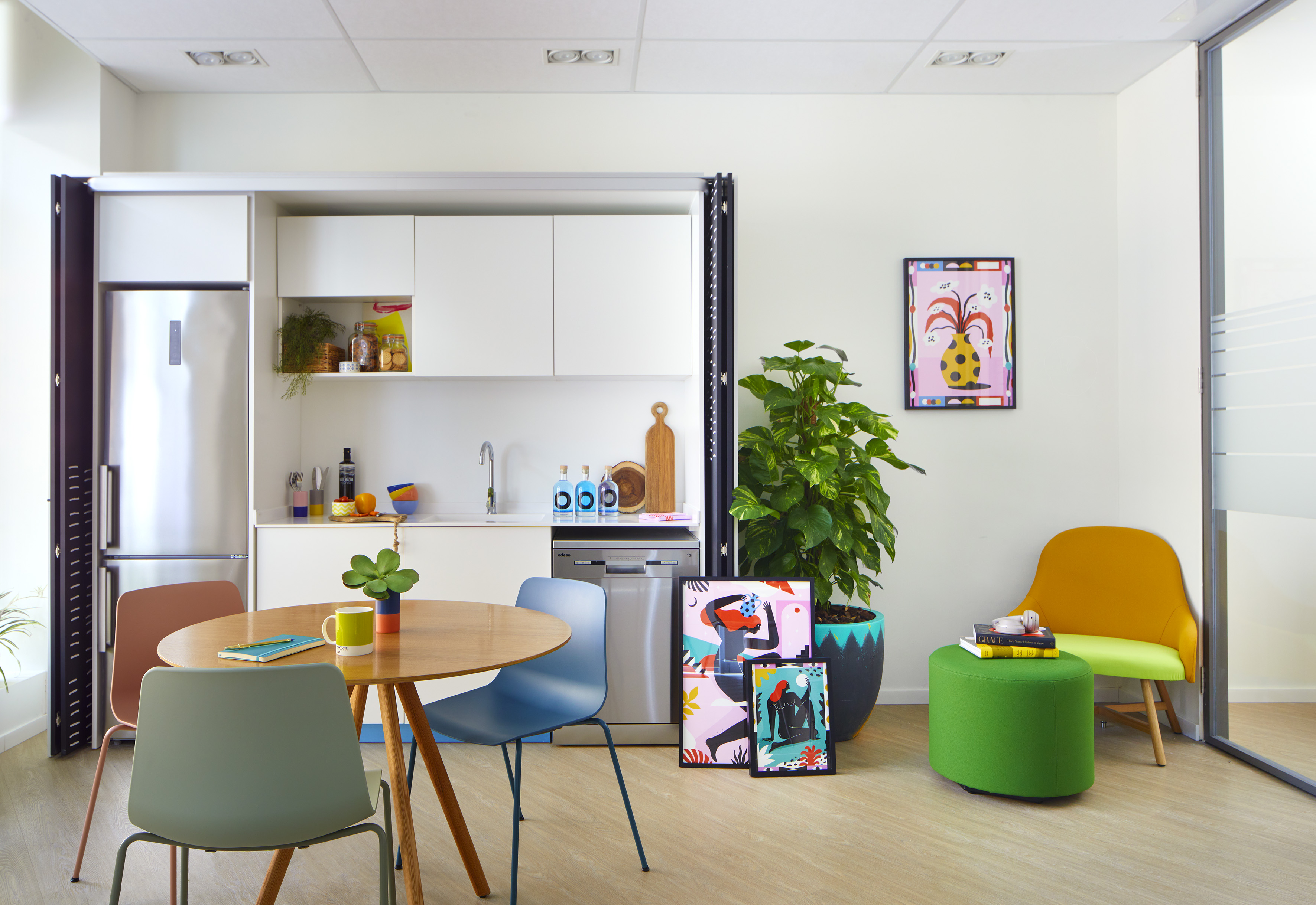 Modern, colorful office breakroom with kitchen, dining table, seating, and vibrant art.