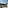 Panoramic balcony view of city buildings, green trees, and distant sea.
