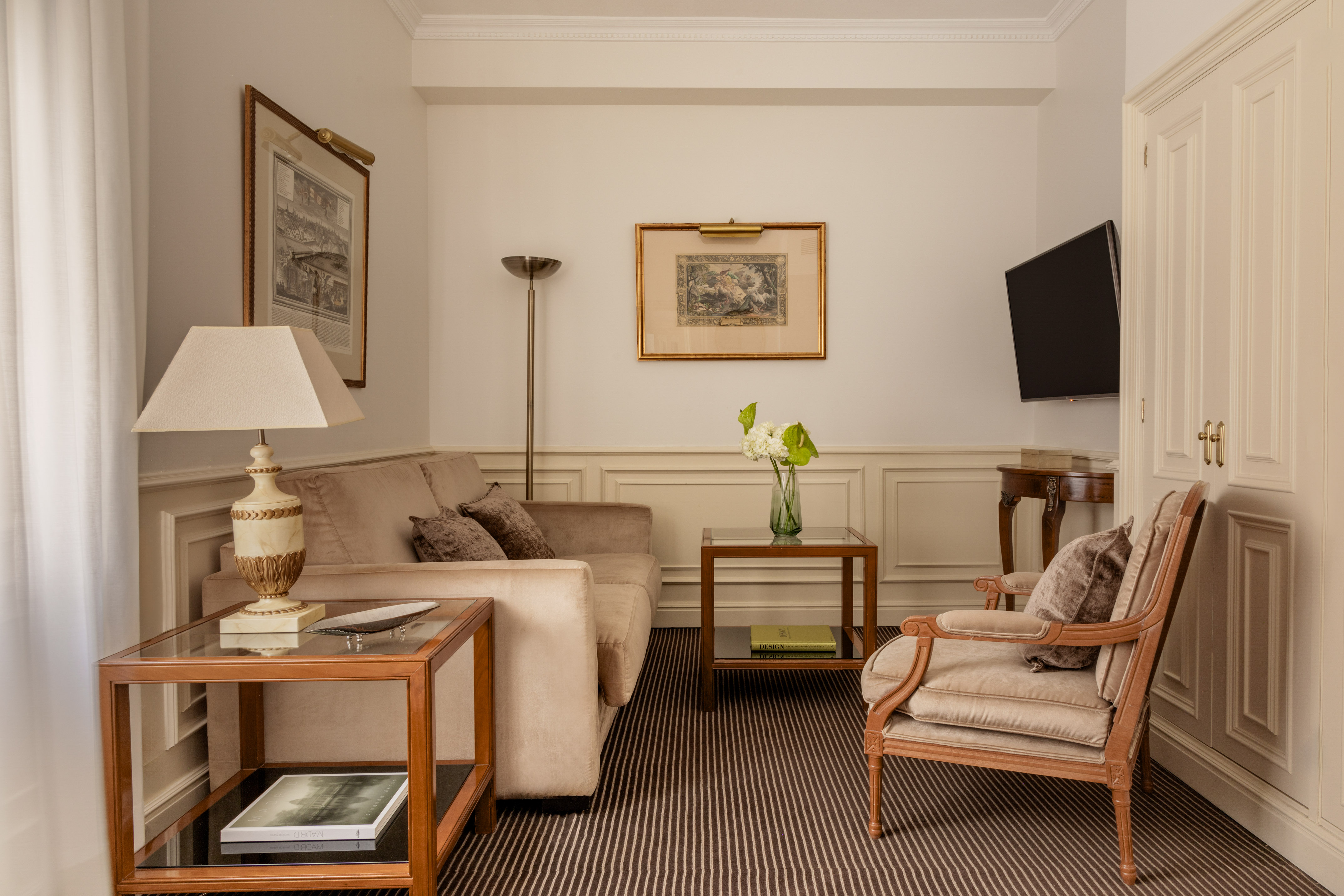 Elegant hotel suite with beige sofa, armchair, and brown striped carpet.