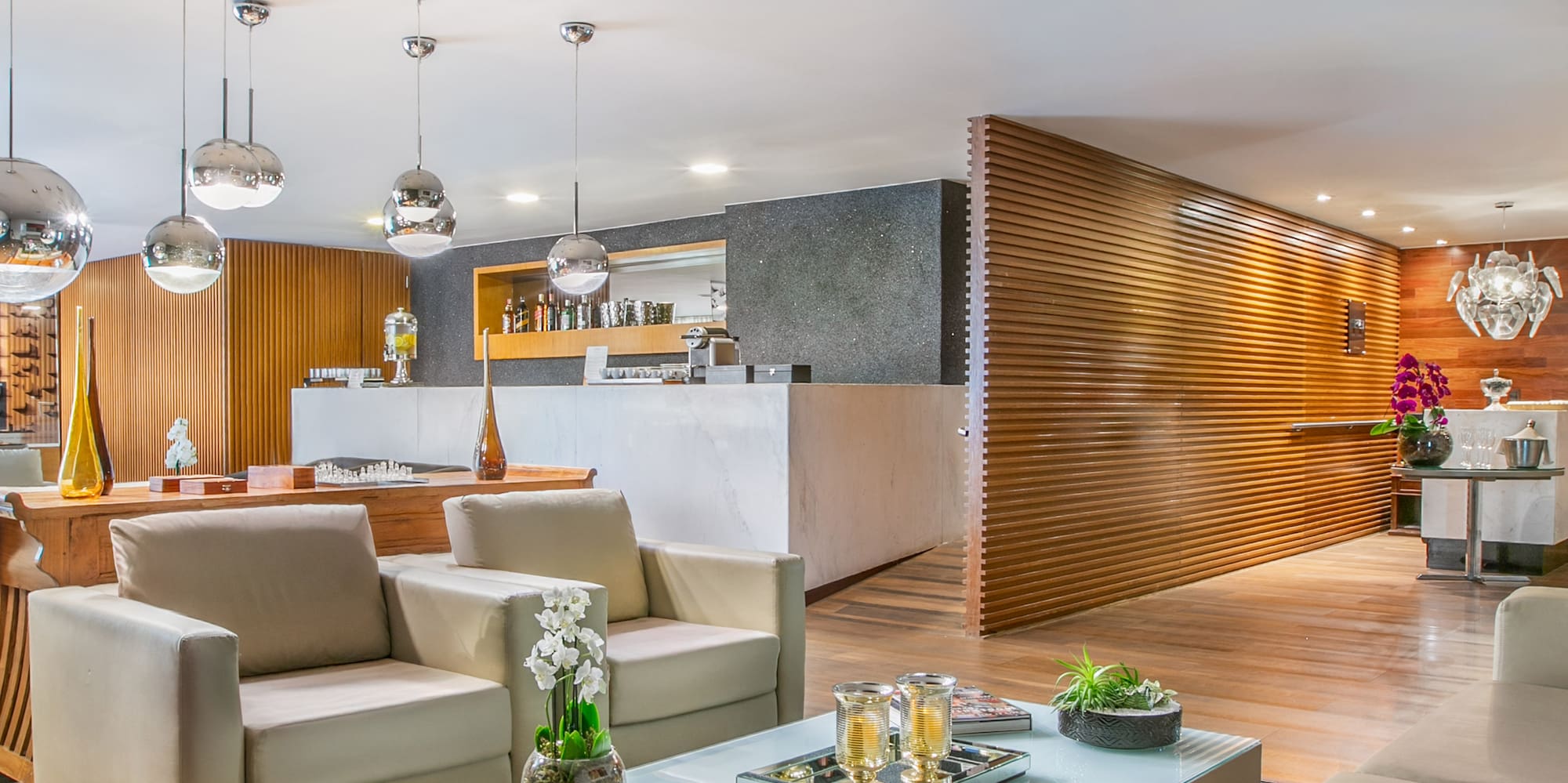 Modern lounge with beige sofas, glass table, striped rug, wood paneling, bar.