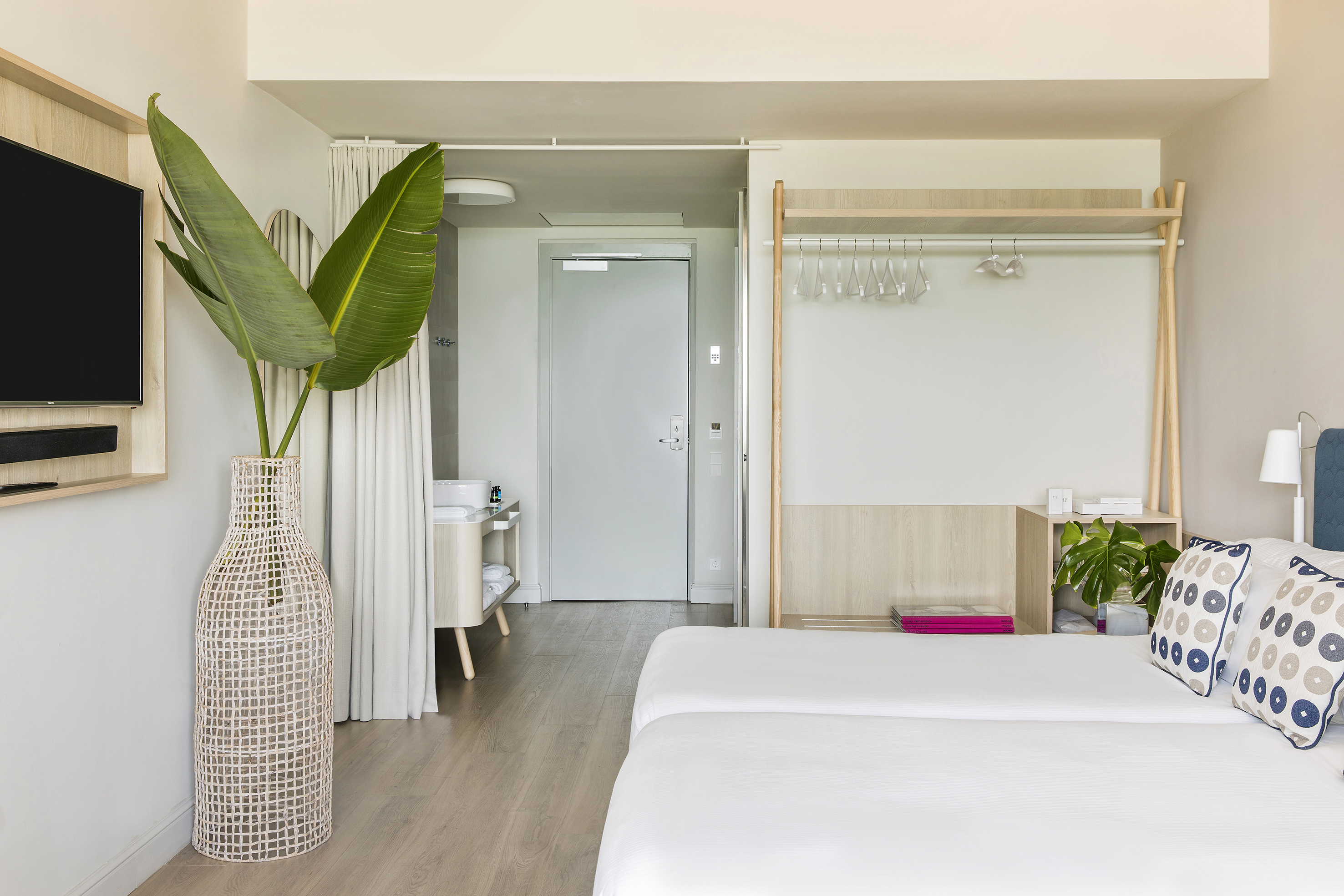 Modern hotel room with twin beds, tropical plant, and minimalist decor.